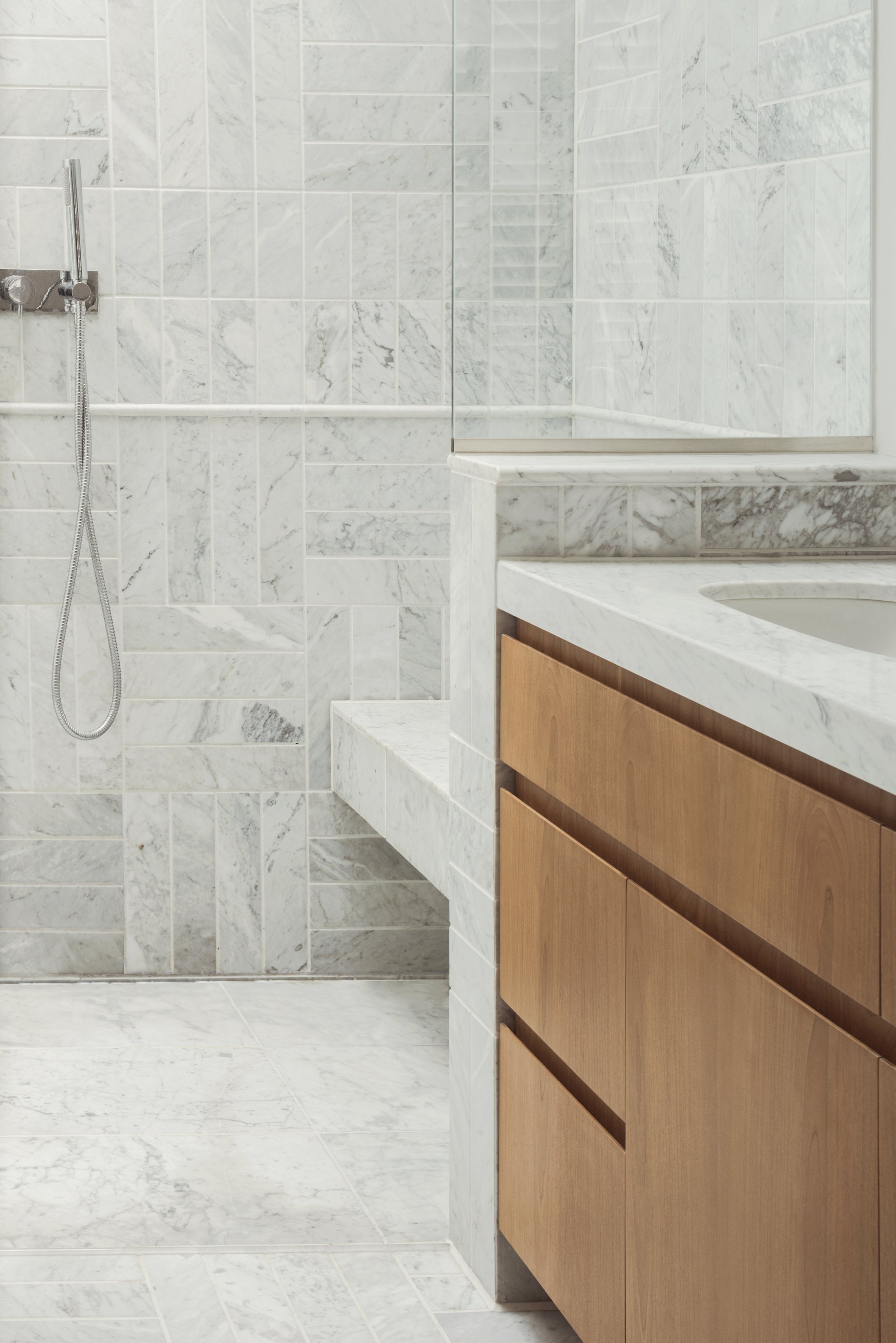 Close-up of a marble bathroom with wood vanity and built-in shower bench.