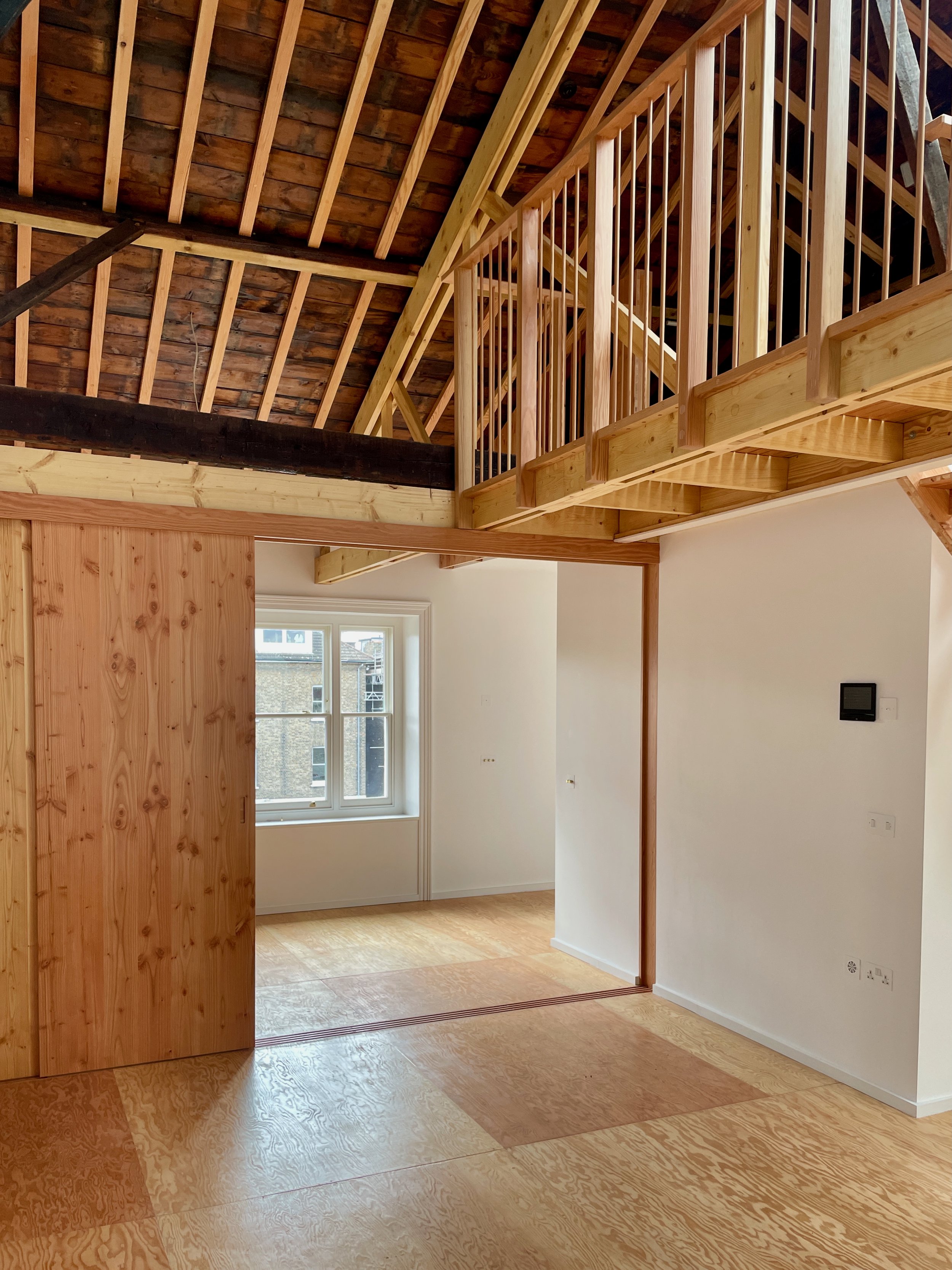 View of loft-style room with pitched ceiling, wood flooring, and natural light from window.