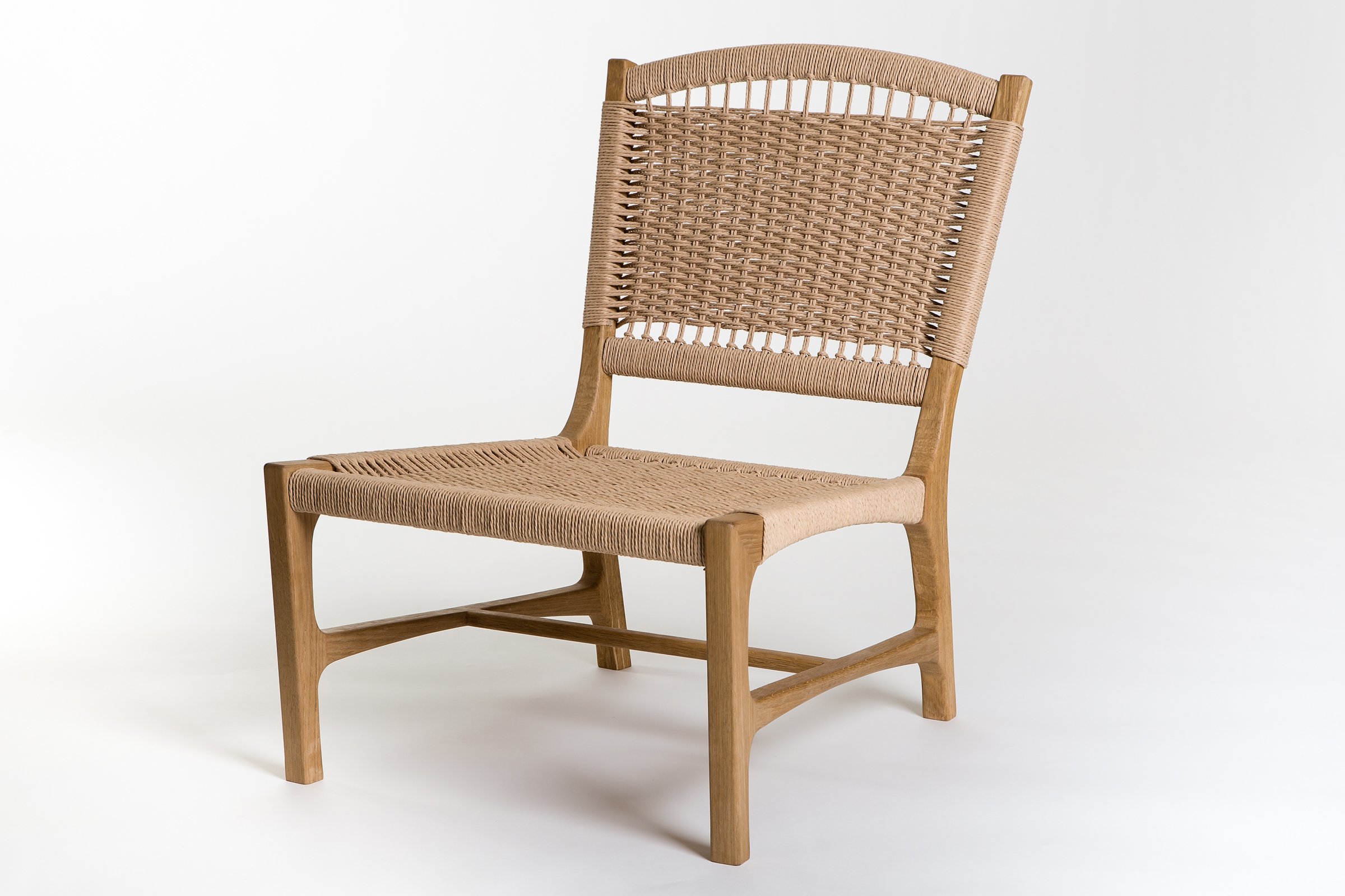Three-quarter view of a wooden lounge chair featuring a sculpted frame and intricate woven seat and back, displayed in a studio setting.