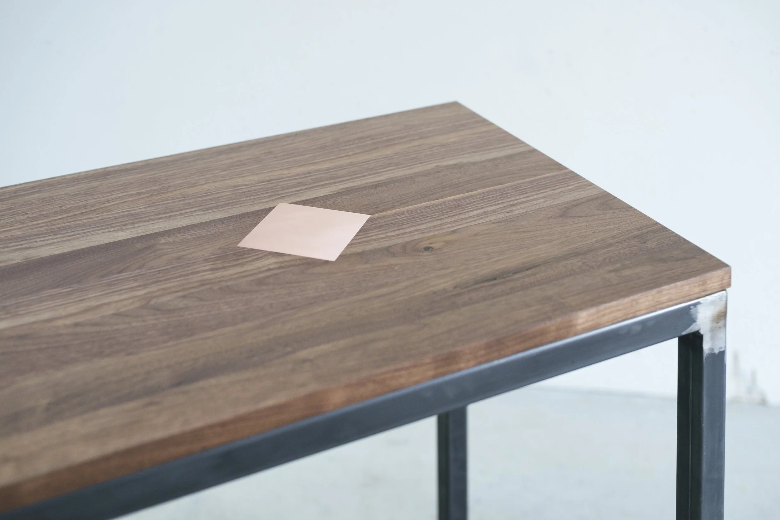 Zoomed-in corner view of the bench, emphasising the wood grain, copper inlay, and raw metal leg joint.