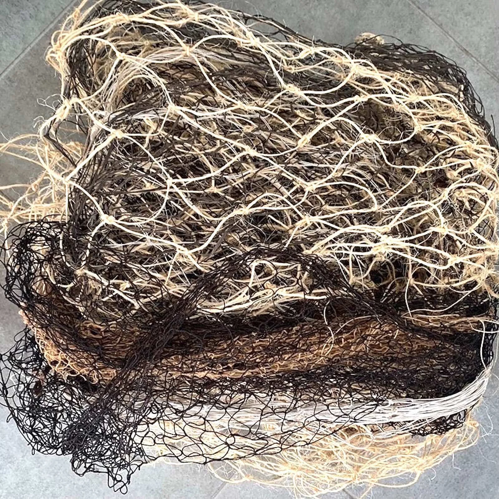 Several nets made of different fibres are flded together in a bundle.  The colours vary from black, to golden through to light cloured sisal and cotton yarns