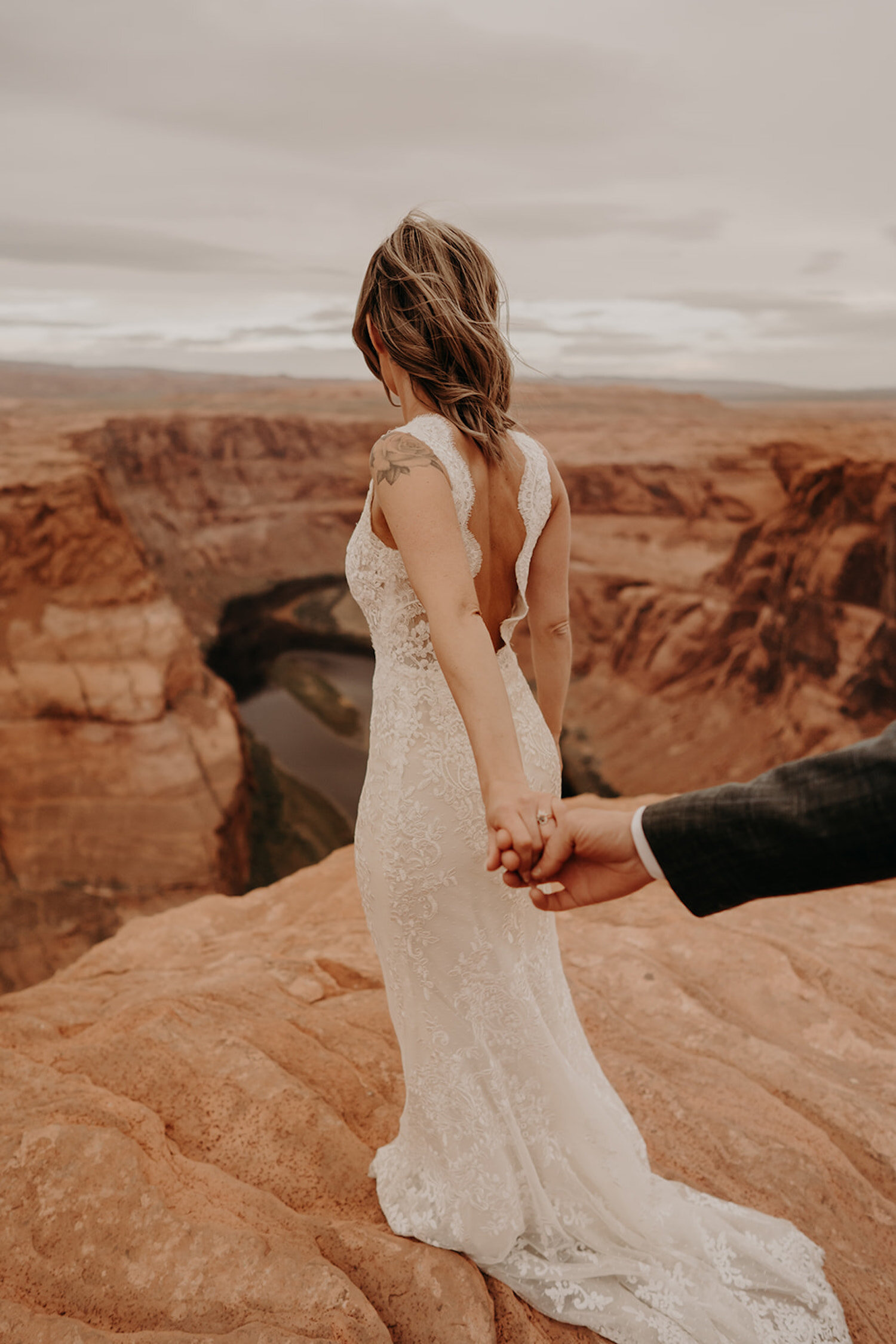 Bride holds grooms hand as she stands on the edge overlooking Horseshoe Bend
