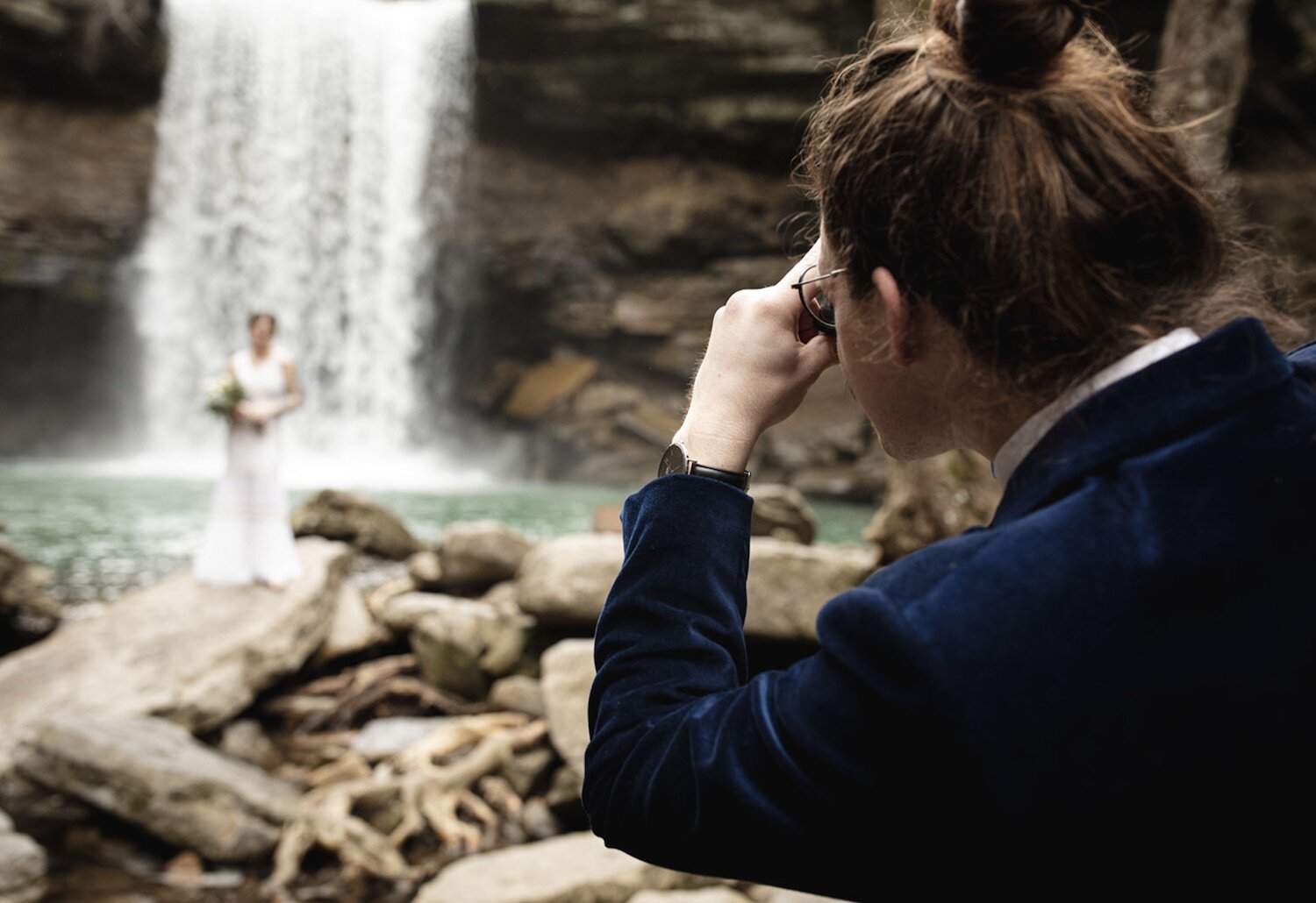Groom takes a photo of the bride as she stands in front of a breathtaking waterfalls