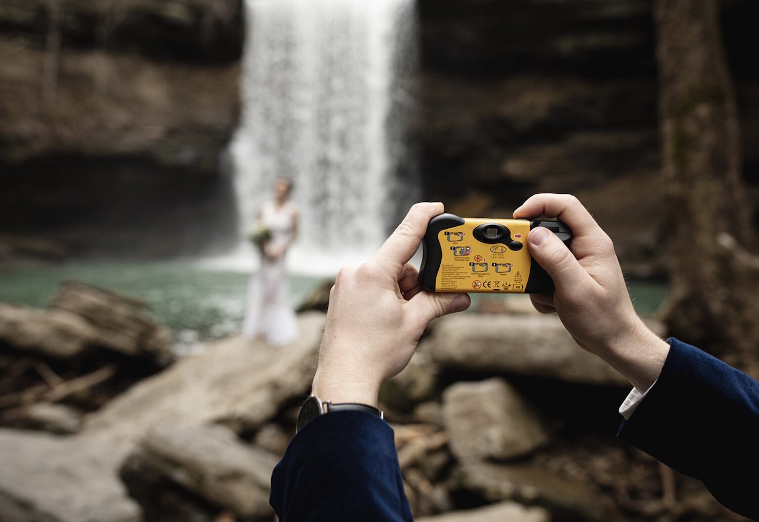 Groom snaps a photo of the bride at a beautiful waterfalls location with a polaroid camera