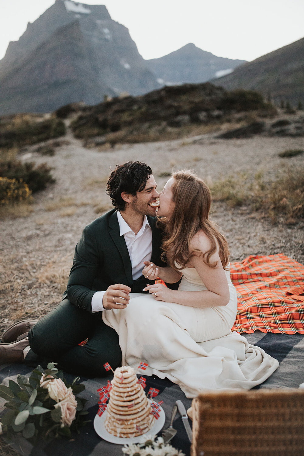 Bride and groom playfully bite into a piece of their food during their Montana elopement picnic