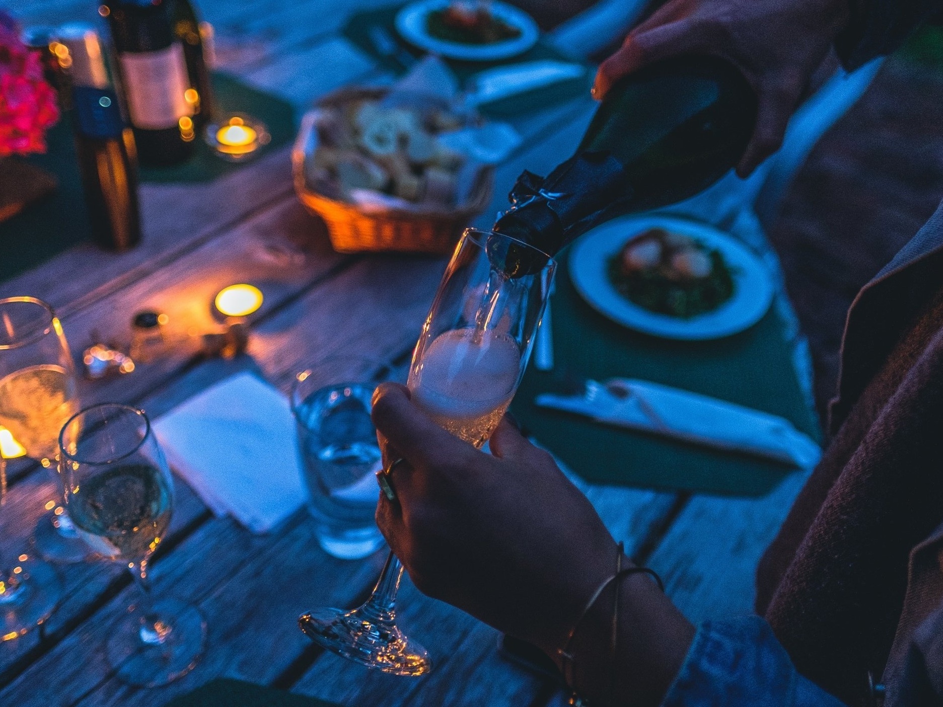 A woman pours wine above a rustic table laid with candles, flowers, and dishes.