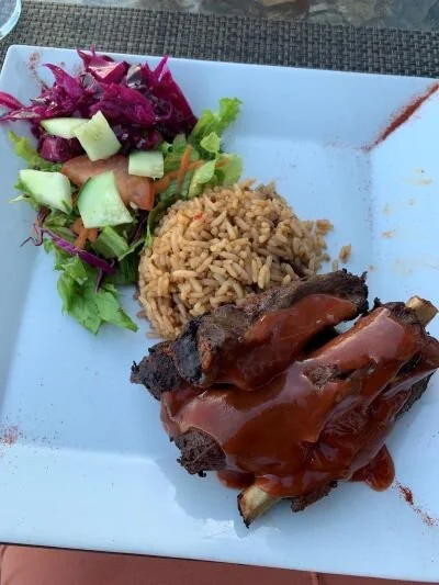 Antiguan ribs, rice, and salad on a white plate.