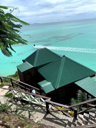 Steps lead down to a green-roofed building by the water while a person rides a jet ski across the waves at COCOS Hotel.