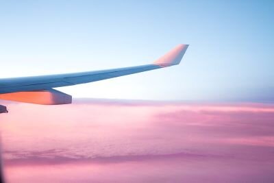 The wing of an airplane, lit from below by the setting sun, juts out over a sea of pink clouds.