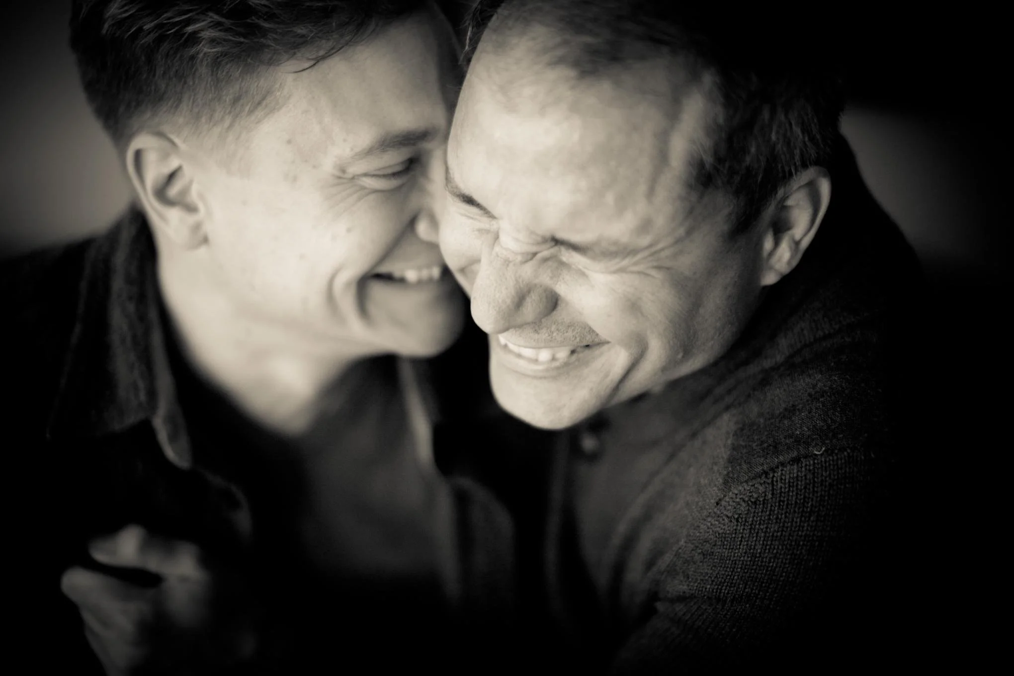 Two men smiling and leaning face to face in a close, intimate moment, black-and-white photo.