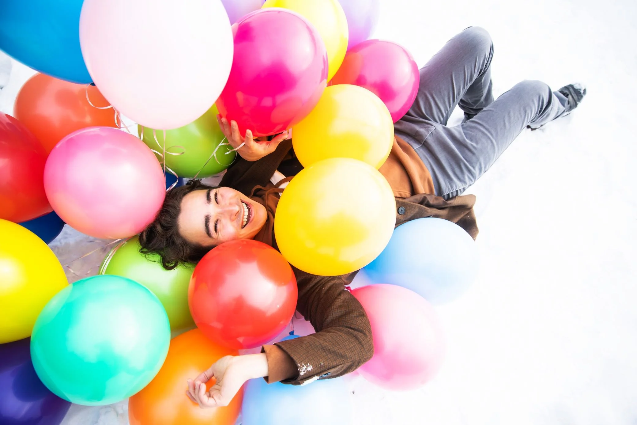 A man lying on the floor surrounded by colorful balloons, smiling joyfully.