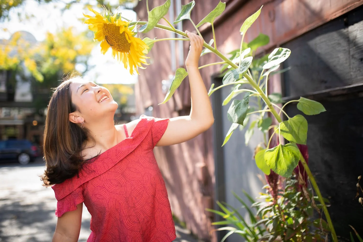 Woman smiling happily as she touches a tall sunflower on a sunny day outdoors.