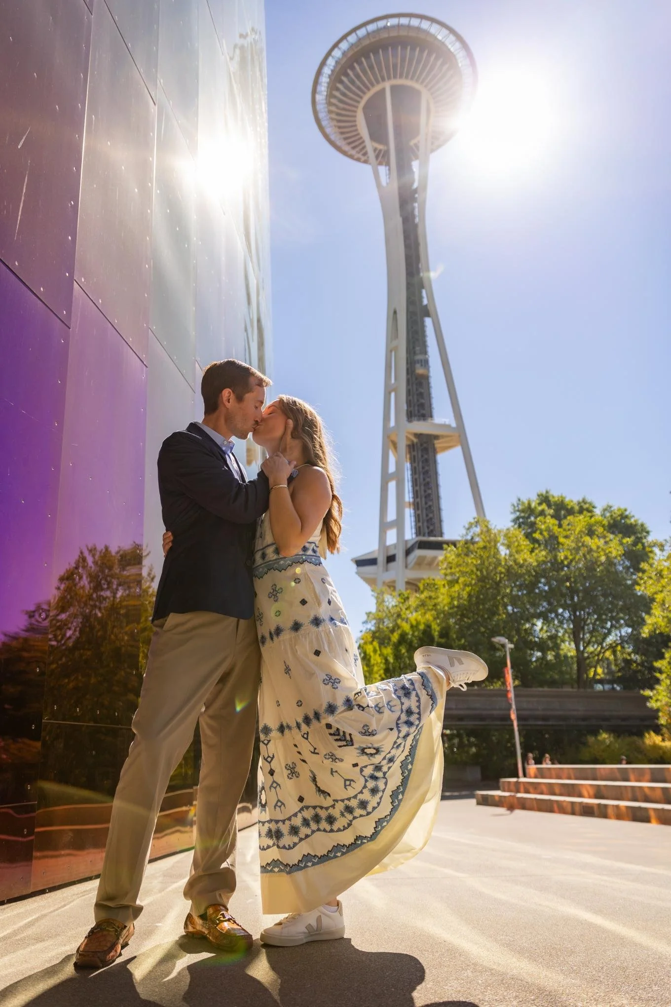 A couple kissing outdoors near the Space Needle in Seattle on a sunny day.