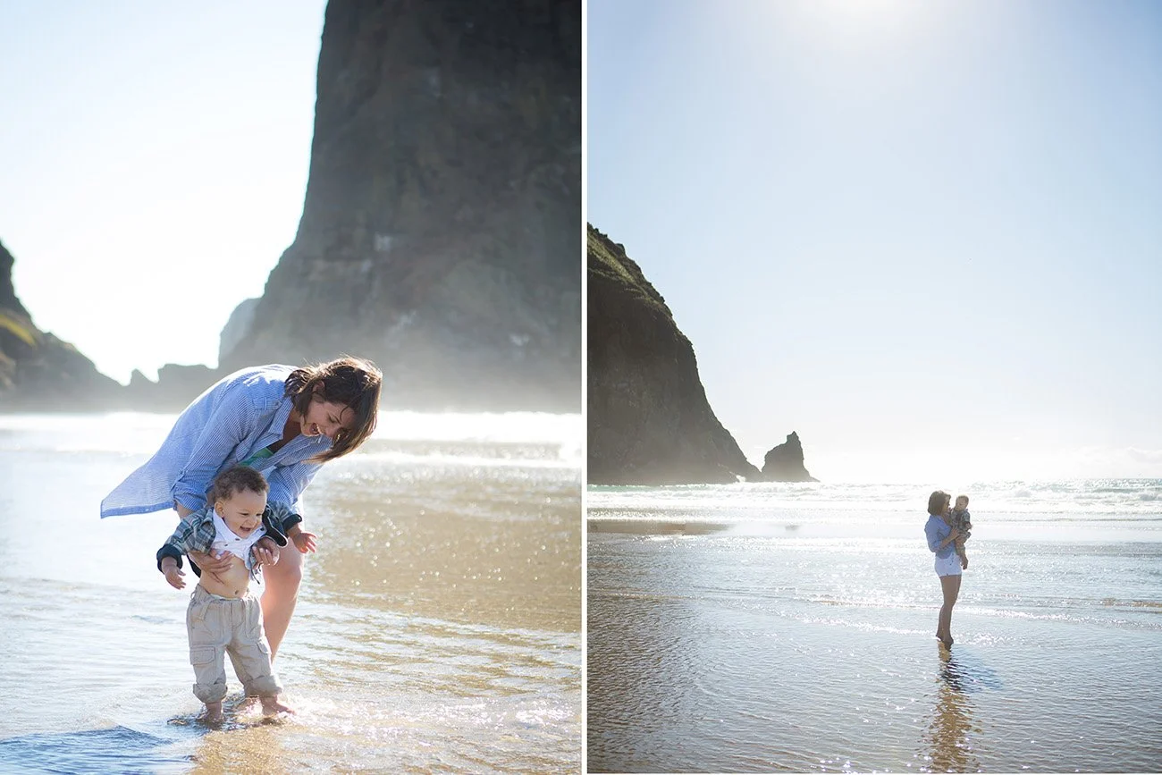 A woman holding a child at the beach with large rock formations in the background, taken during daylight.