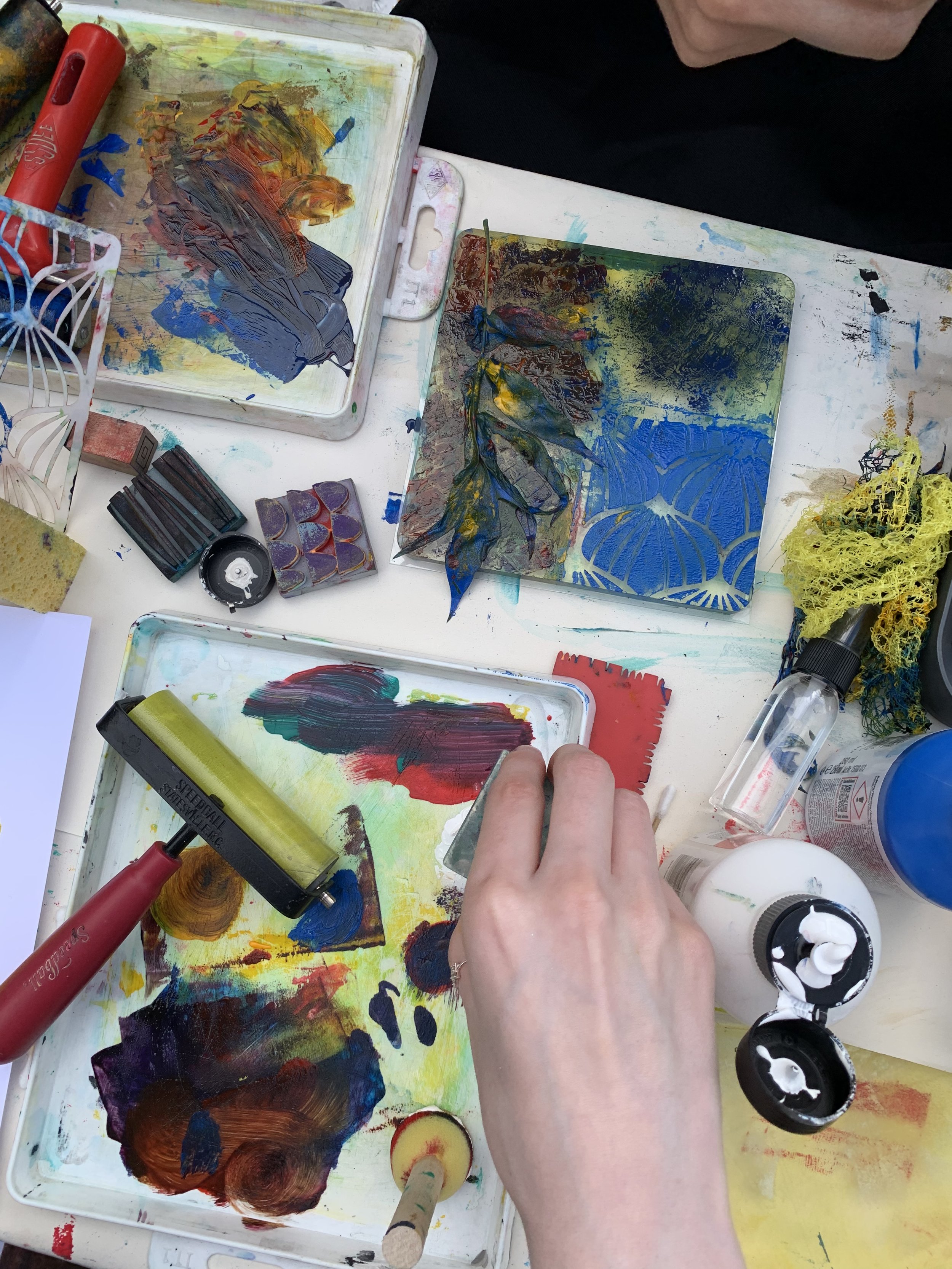 Hand showing using stamps, and textured objects to make gel plate prints