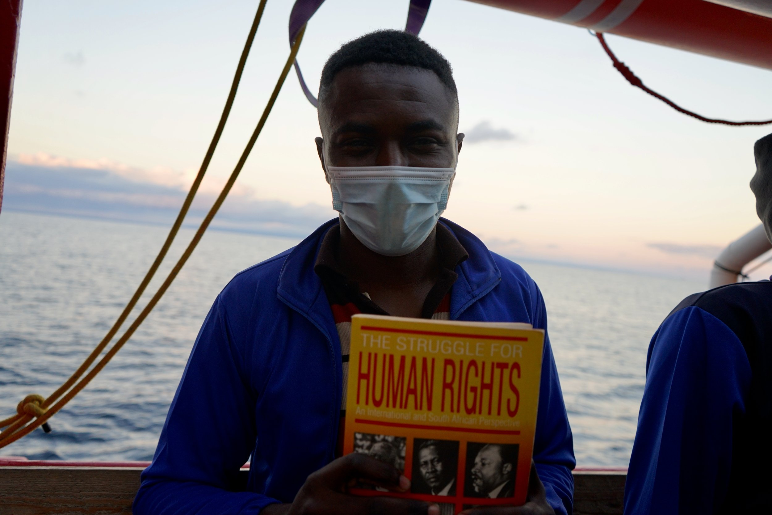 A survivor holds a book in his arms which he has been reading about human rights during the wait for place of safety. 
