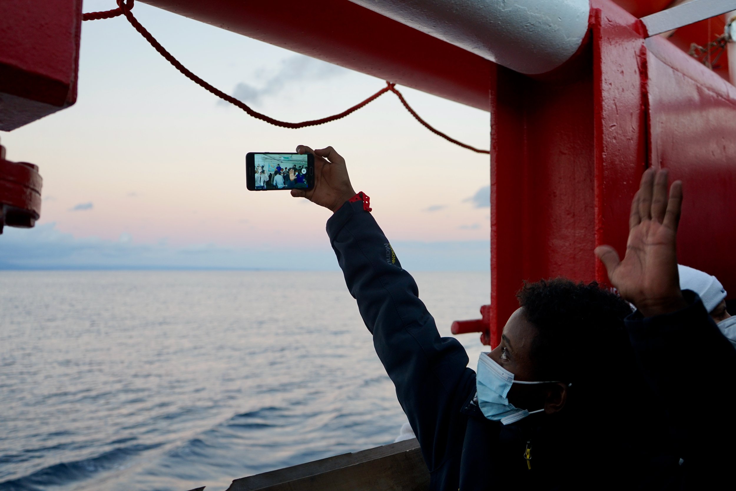 A young man takes a selfie with the cheering survivors on board following the announcement for a place of safety. 