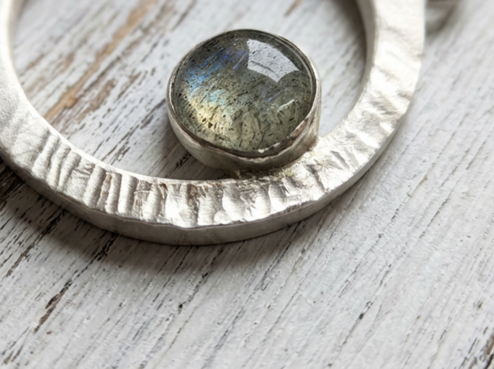 Close-up of hammered silver texture and luminous blue-green flash in bezel-set labradorite stone.