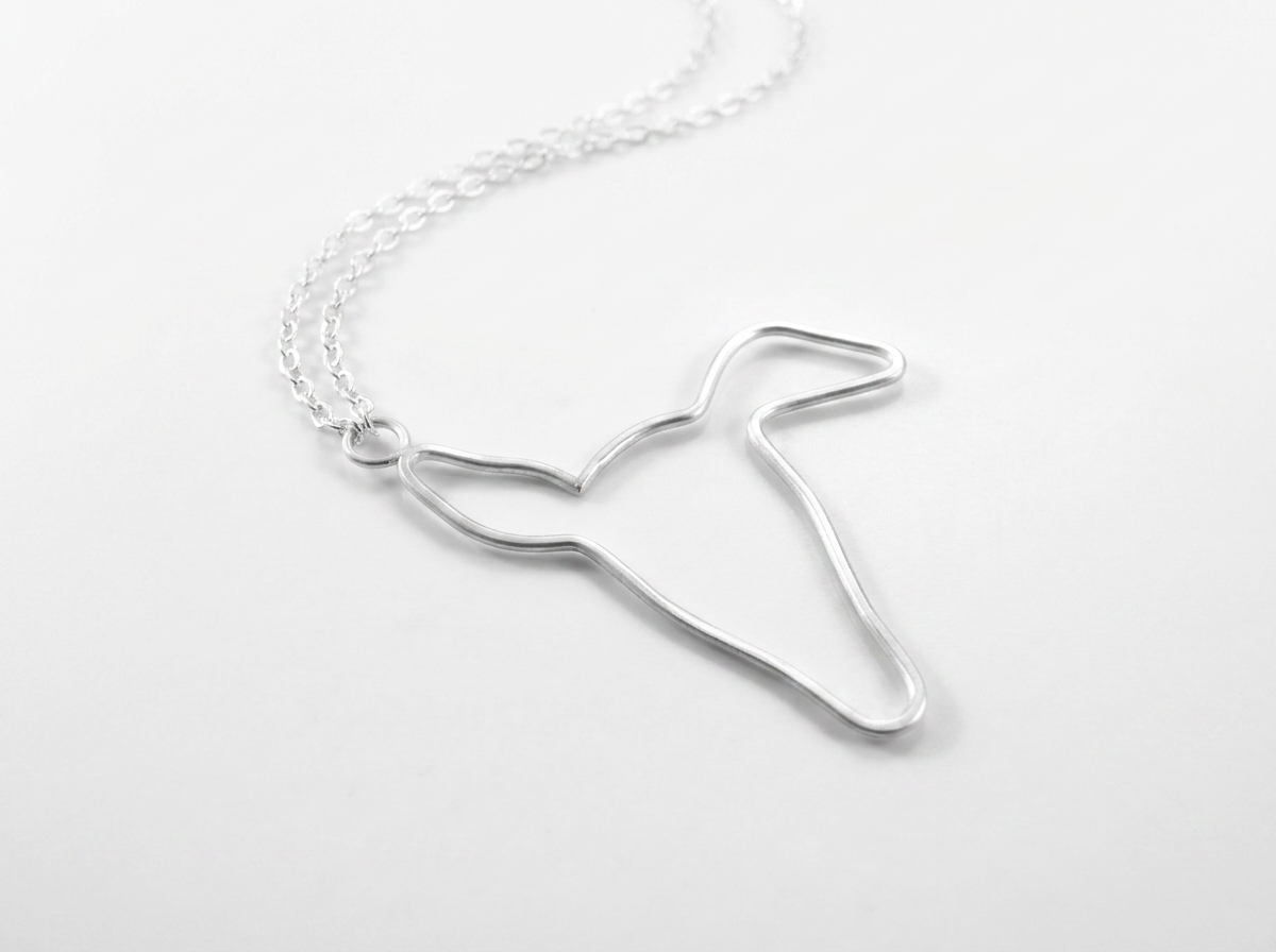 Close-up of brushed satin silver greyhound pendant showing fine hand shaped silhouette details.