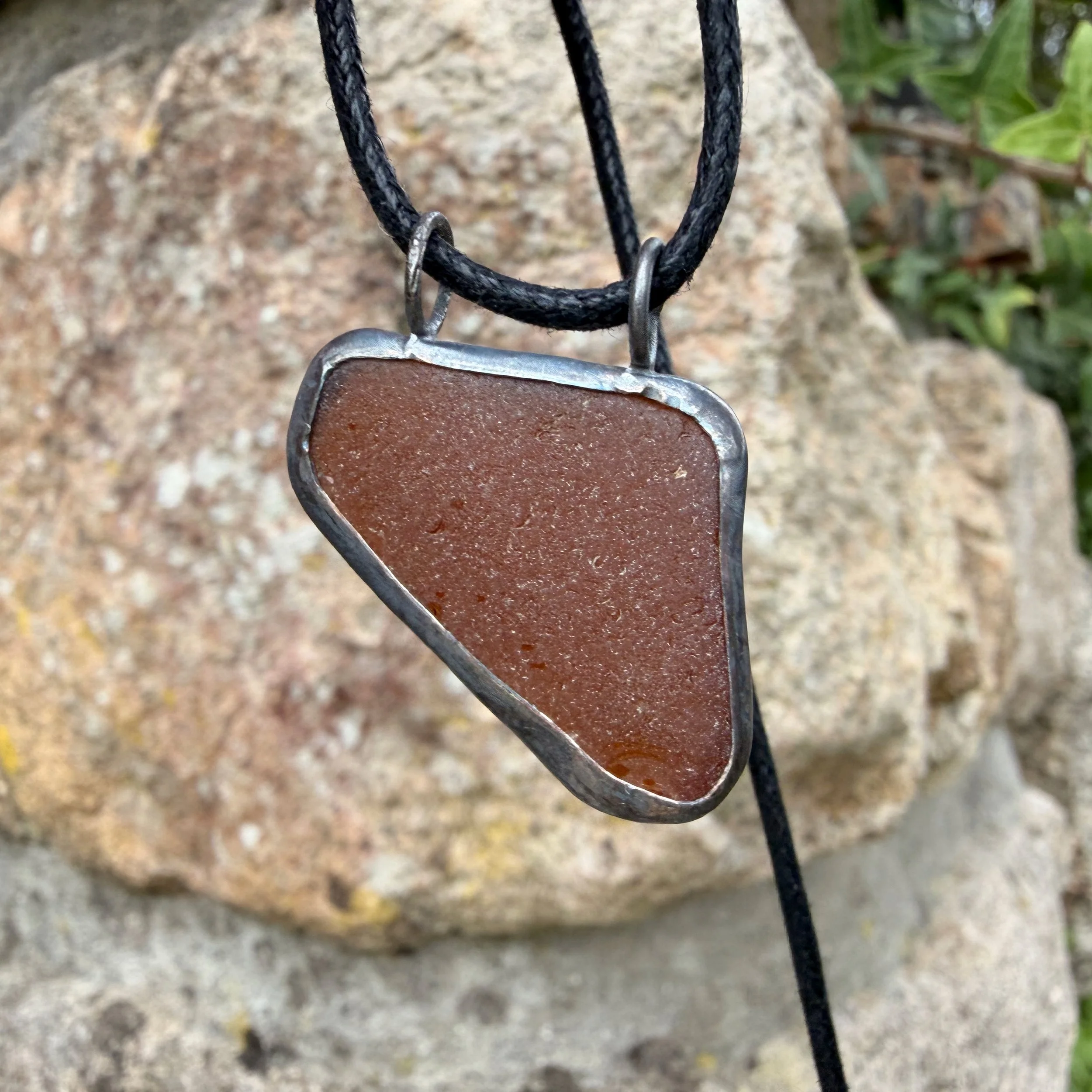 rugged brown sea glass pendant photographed outside showing the deep amber brown hue
