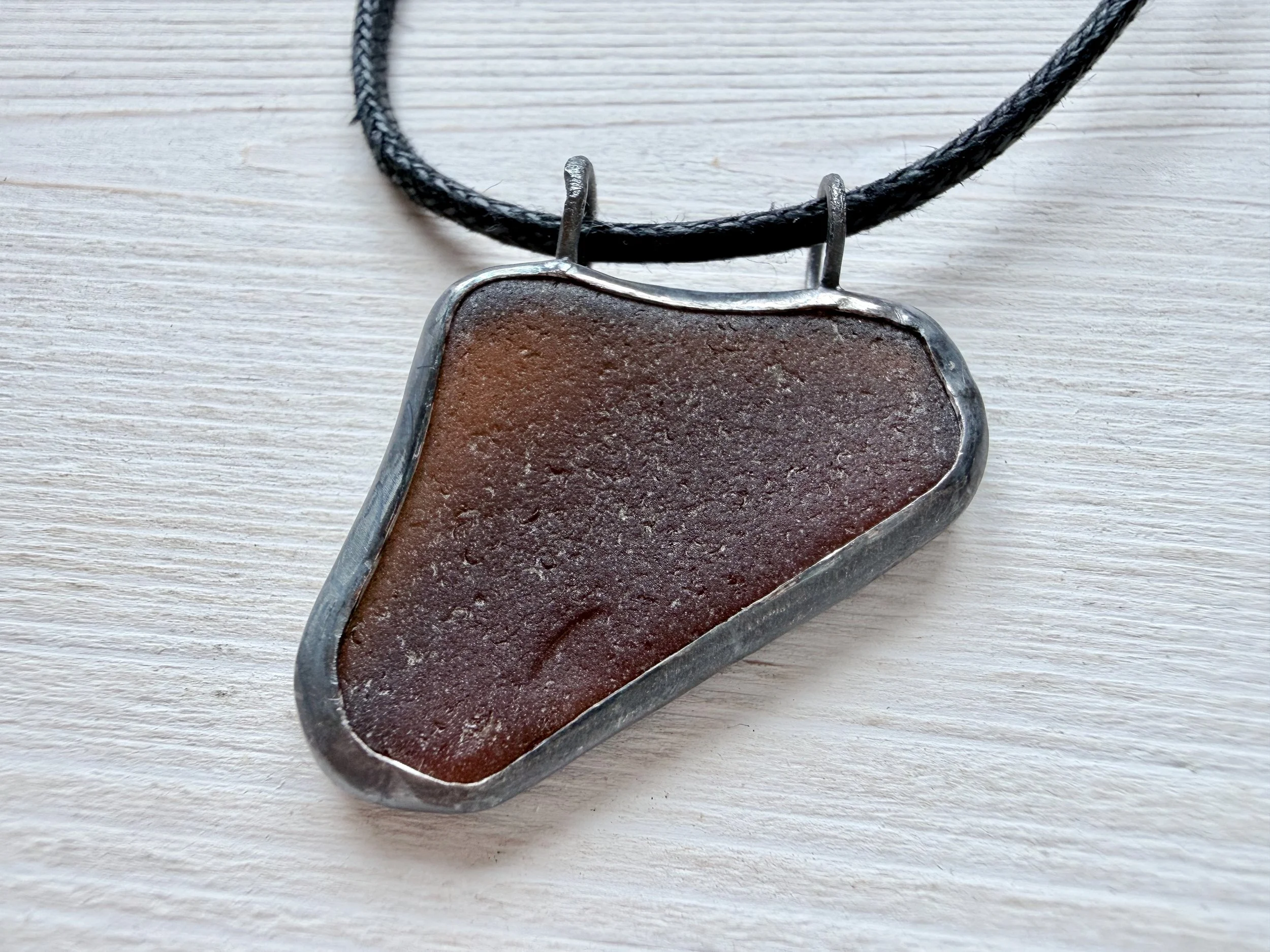 Close-up of triangular brown sea glass piece with double top jump rings and antiqued silver finish.