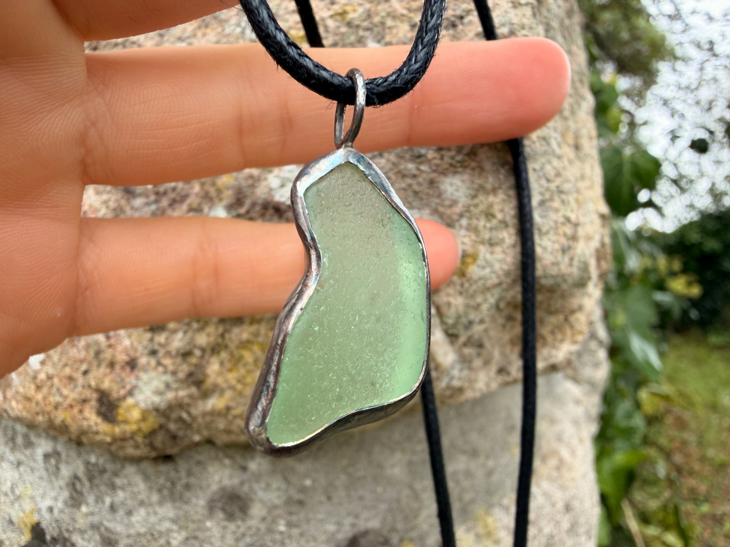 hand hoding a sea foam green handcrafted sea glass pendant showing the glowing colour