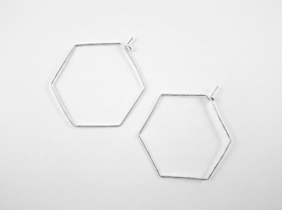 Pair of handcrafted geometric recycled sterling silver hexagon hoop earrings with hammered surface detail.