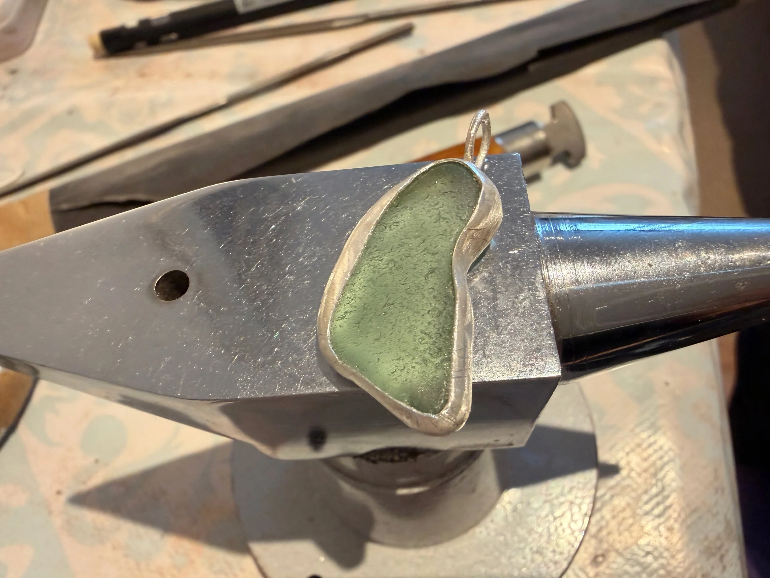 handcrafted sea glass sea foam green pendant being set on a small anvil