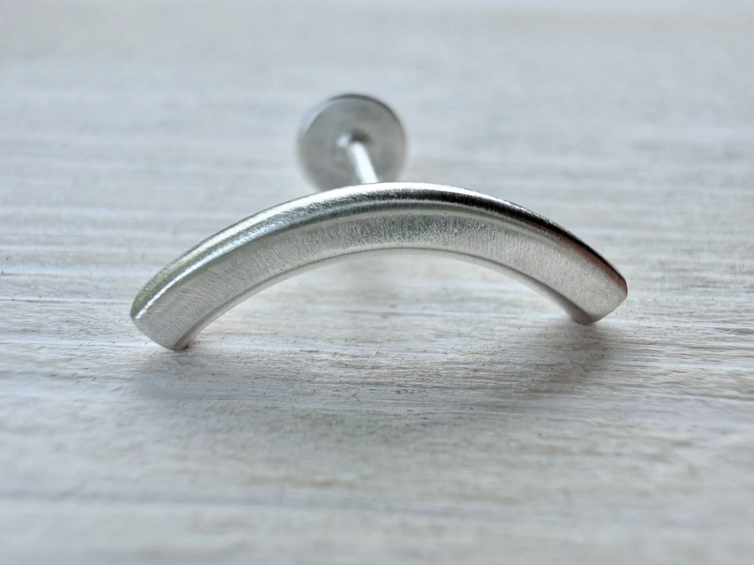 Handcrafted recycled sterling silver minimalist satin curved bar conch stud earring on white wood background.