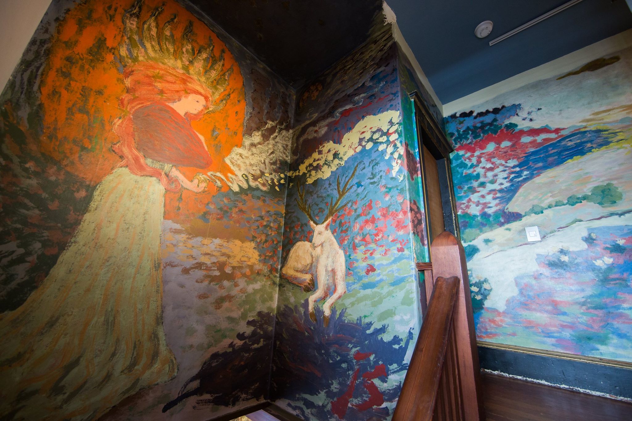 Hallway mural by Jess picturing a deity with her hair on fire, a stag and a mystical medieval romantic fantasy world that continues down the corridor. 