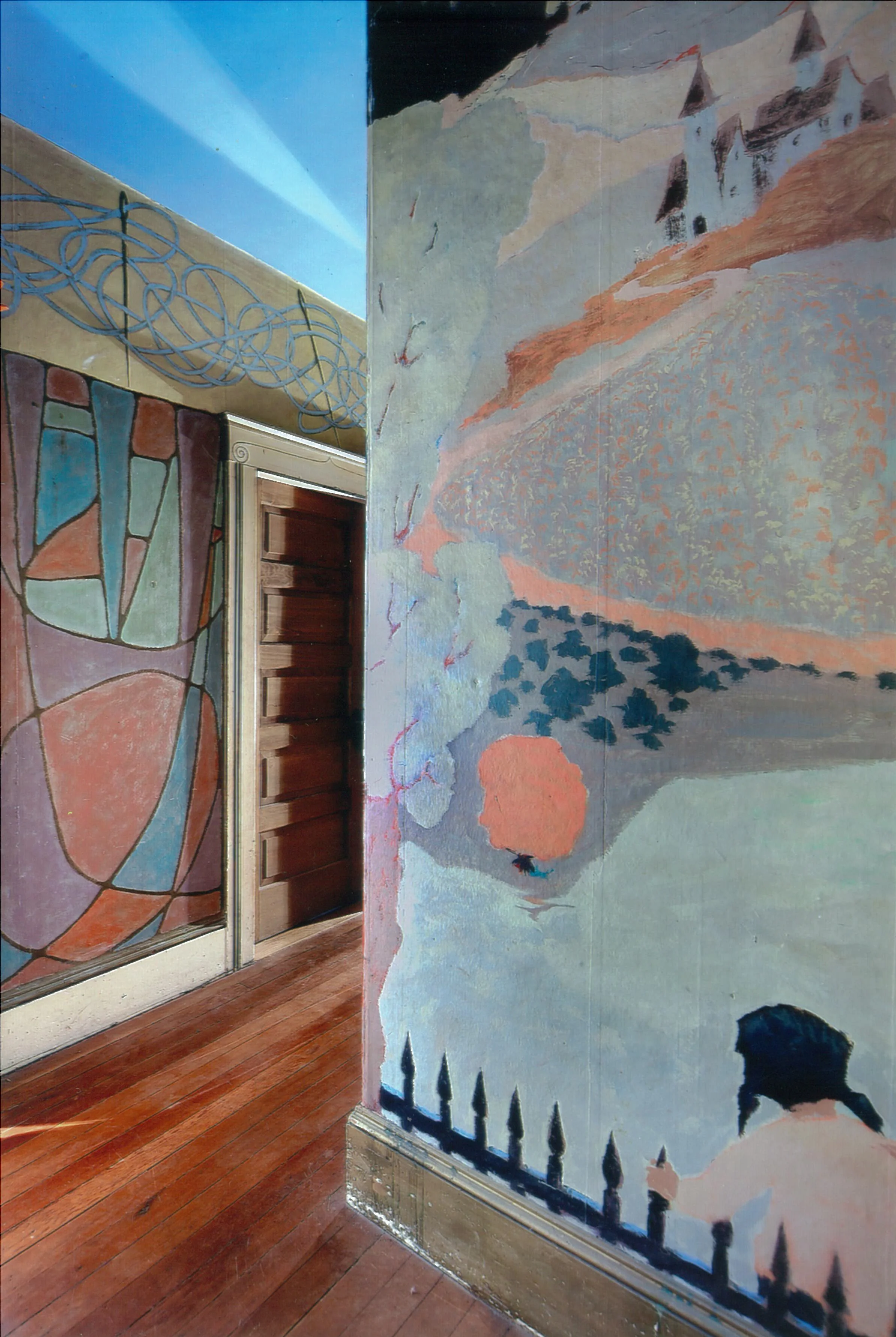 Jess hallway mural continued, picturing a girl looking over an iron fence at pale green fields and a distant castle atop a mountain. 