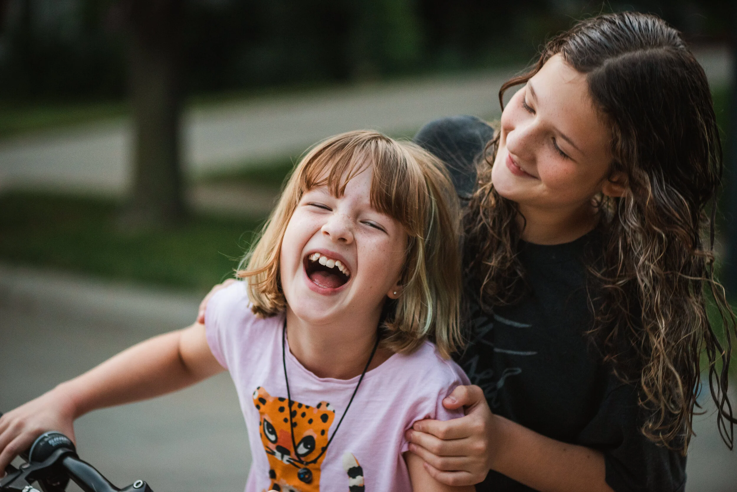 Two girls outside laughing on a bicycle.