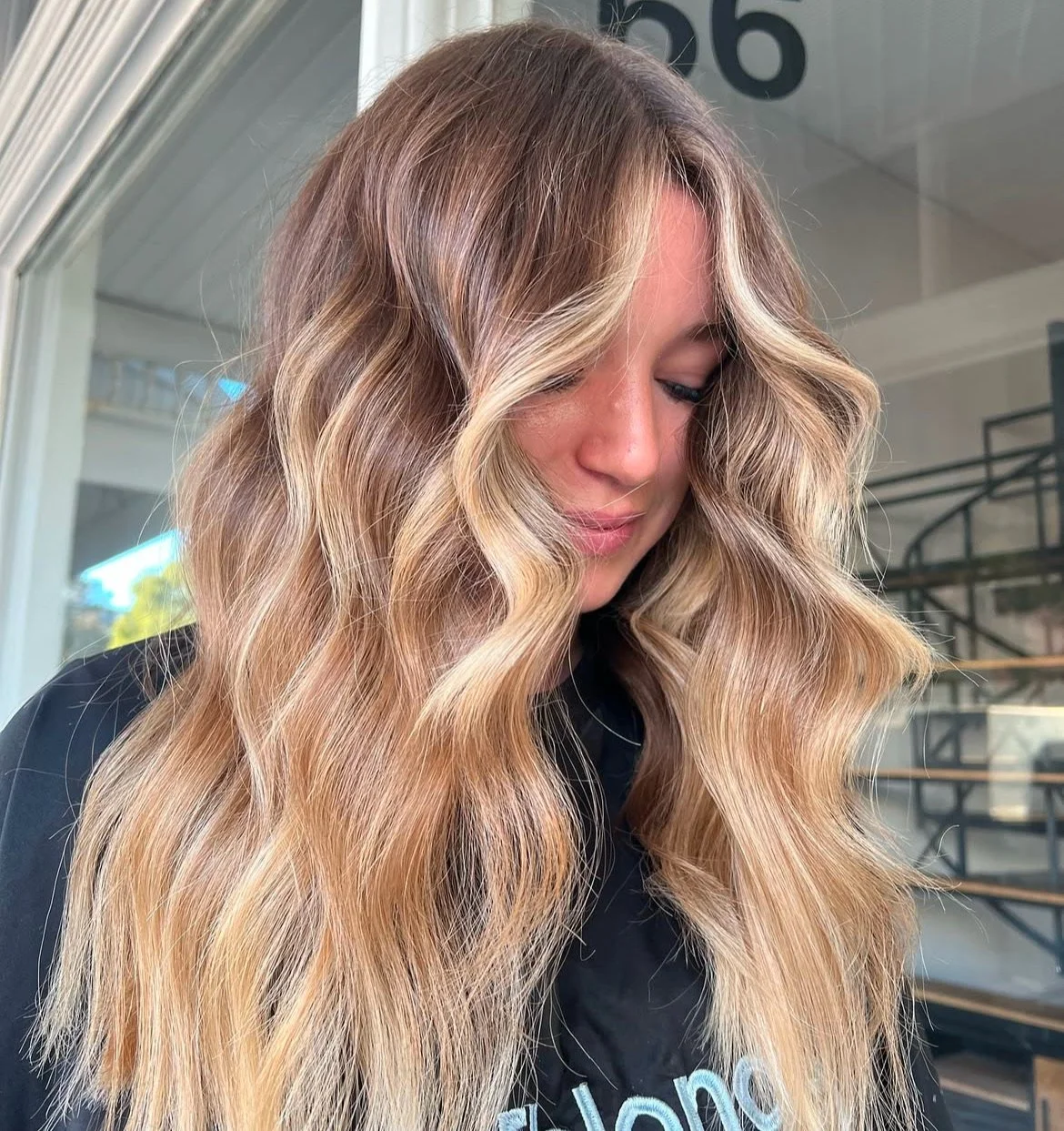 A woman with long, wavy blonde hair looking downward in a salon setting.
