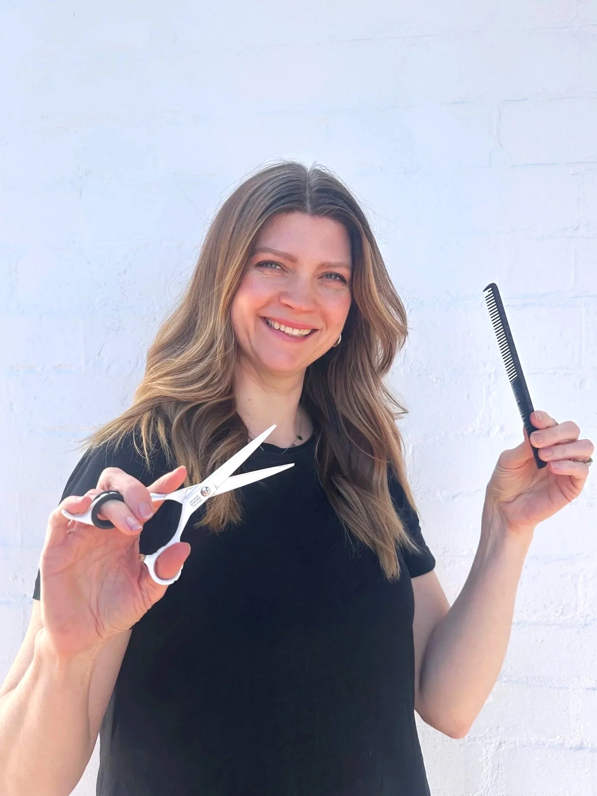 Smiling woman with brown blonde hair holding scissors and comb