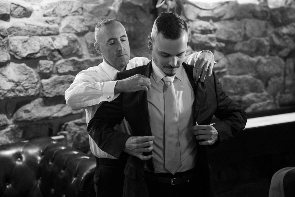 Groom putting on jacket in the man cave at Deer Creek Valley Ranch