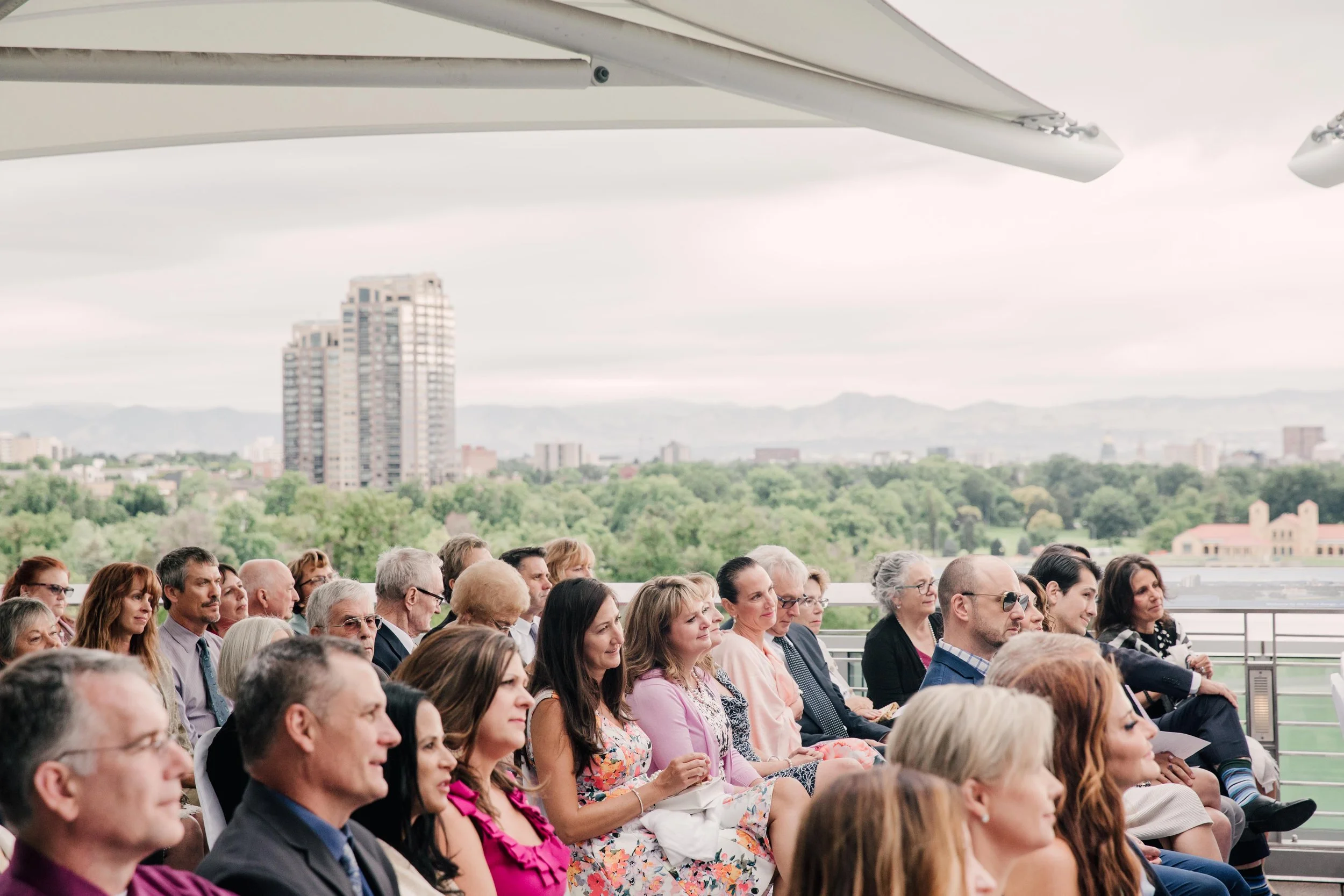 A group of people seated outdoors with a cityscape and mountains in the background, attending an event.