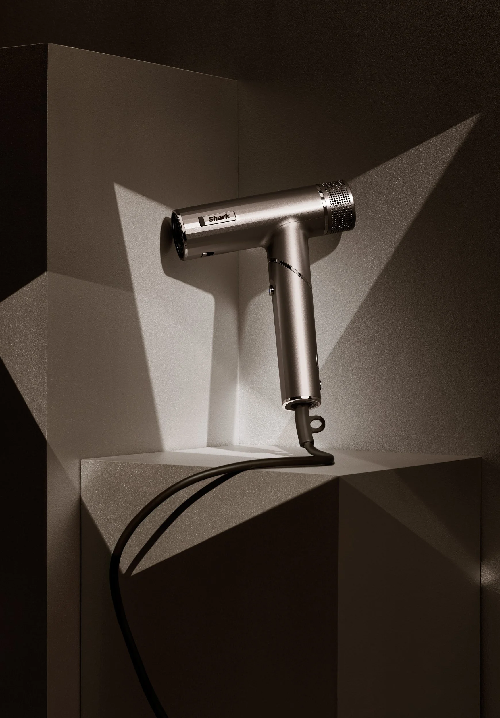 Adam Krauth Photo - Commercial Photography - Boston, MA - Still Life - Product Photography - A metallic Shark hair dryer positioned on a shelf, casting shadows on a textured wall background.