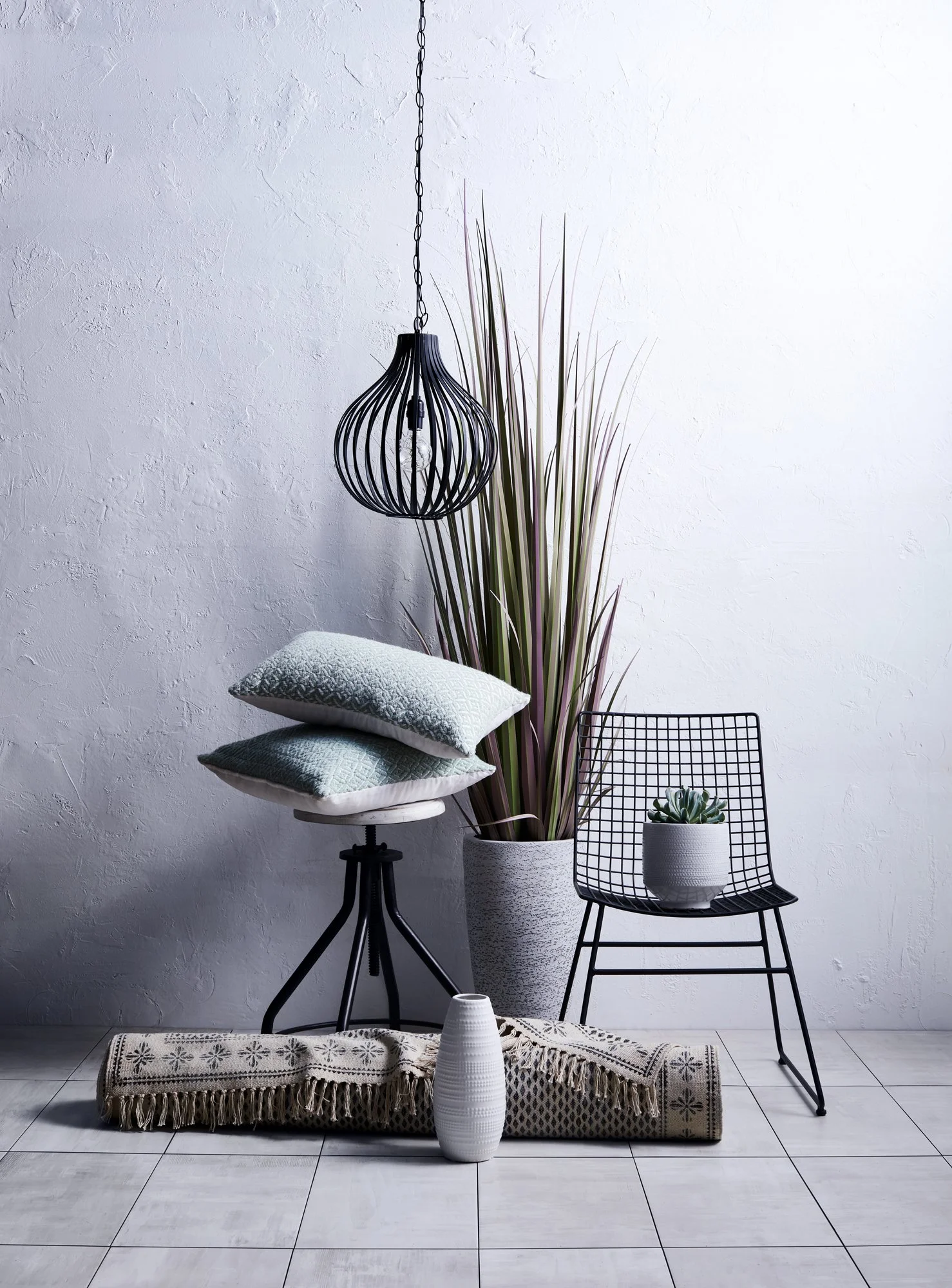 Adam Krauth Photo - Commercial Photography - Boston, MA - Still life - Interior photography. A scene of a minimalist interior space with a white textured wall, a black wire hanging pendant light, a tall potted planting other decorative accessories. 