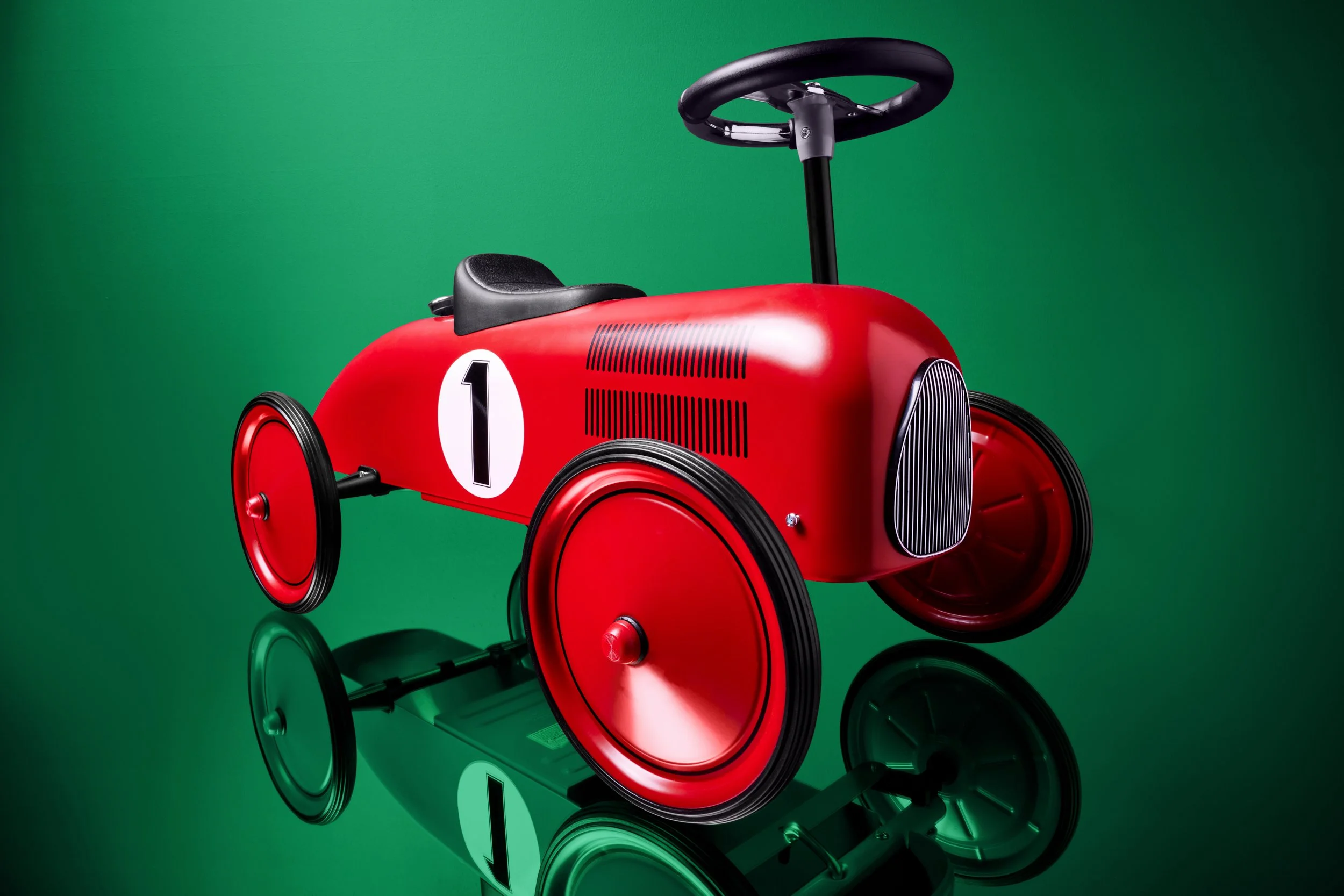 Adam Krauth Photo - Commercial Photography - Boston, MA - Still Life - Product Photography - Red vintage-style pedal car with the number 1 on the side, set against a green background with reflected image below.