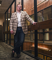 Man standing and leaning on a wooden railing inside a modern office building with glass walls and wooden accents.