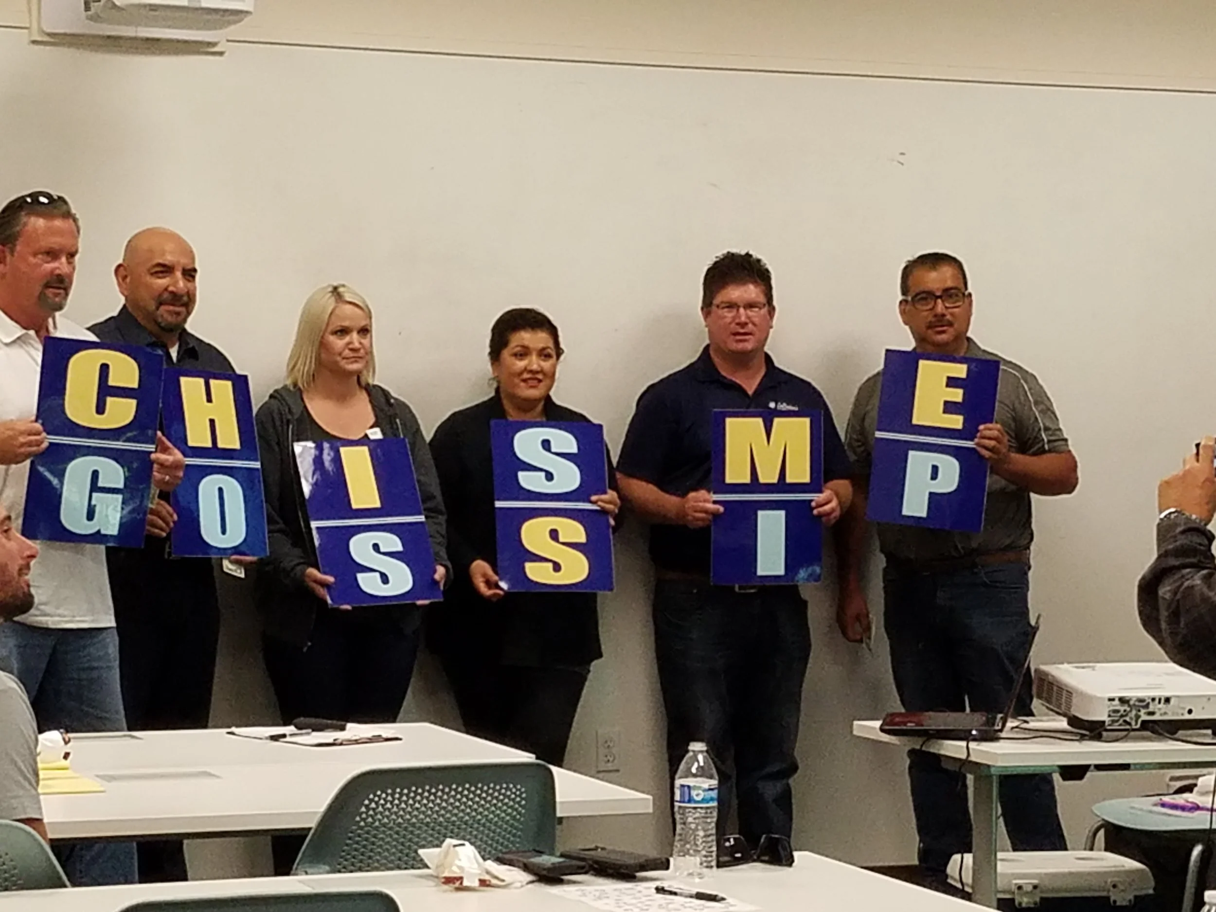 Audience members holding letter signs that spell "Chisme" in Spanish and "Gossop" in English. 
