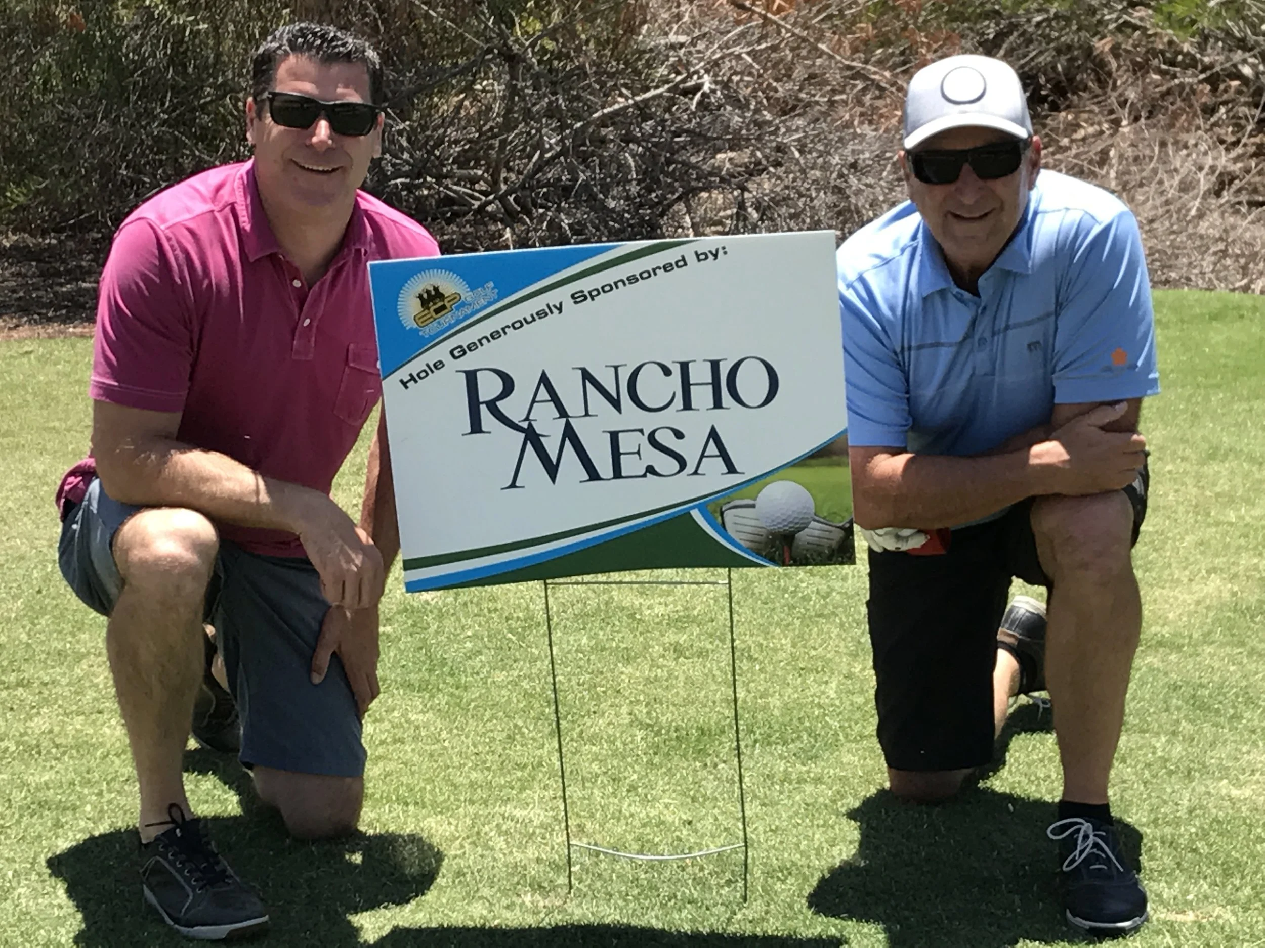 Sam Clayton and Dave Garcia kneel next to the Rancho Mesa Hole Sponsorship sign.