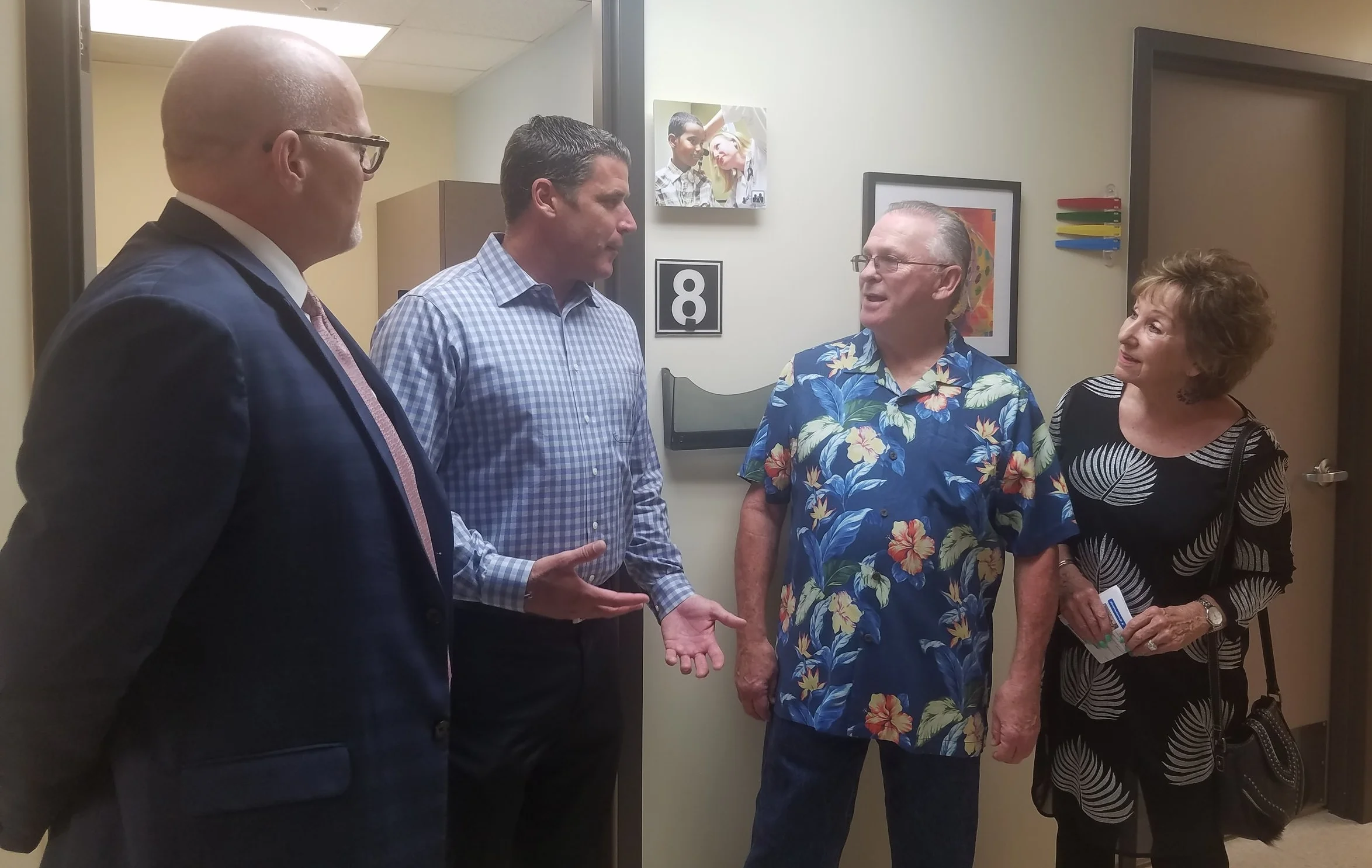 Anthony White, Sam Clayton, Tom and Debby Doyle talking in hallway in front of an examination room at Family Health Centers San Diego.