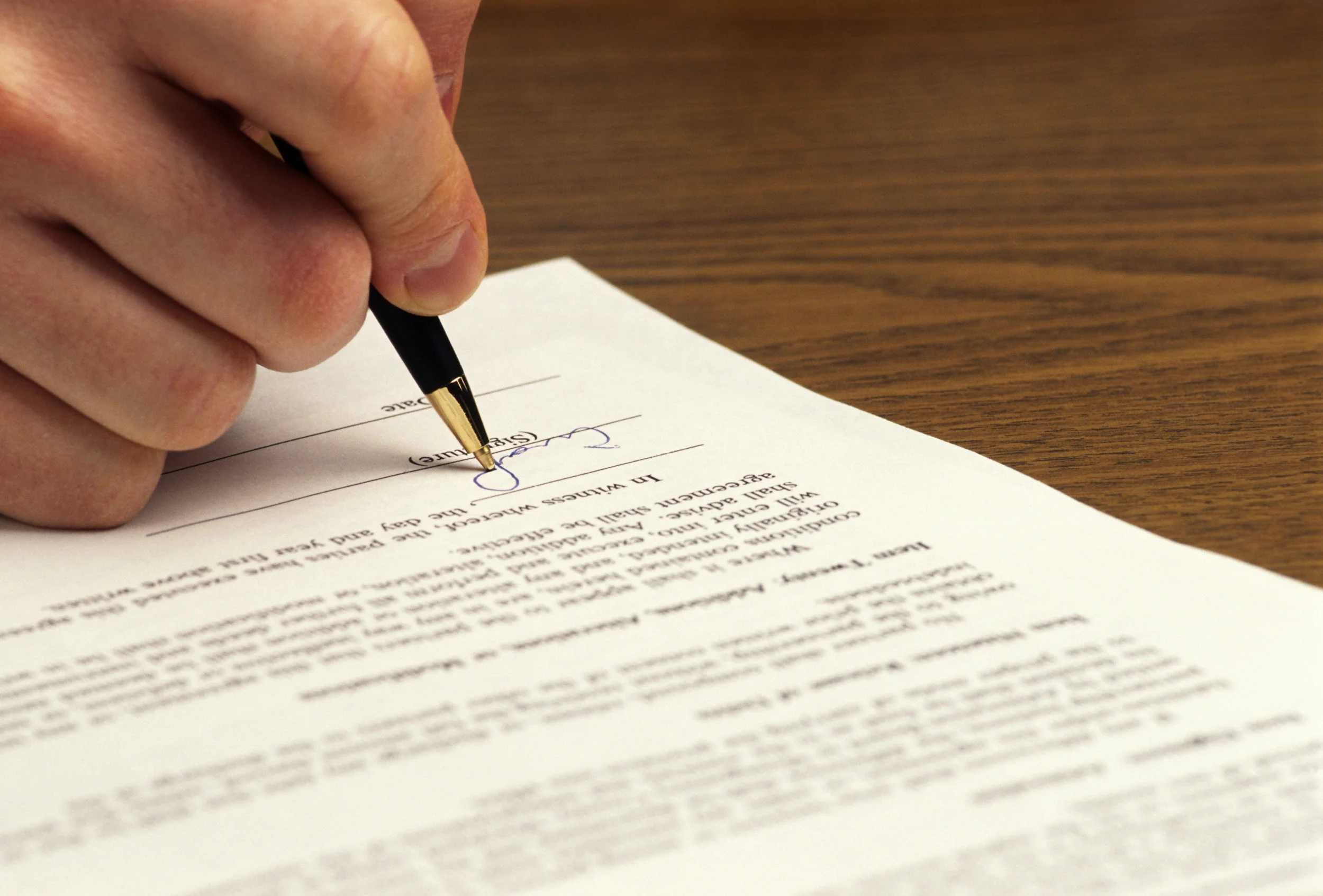 Hand signing a contract with a pen.