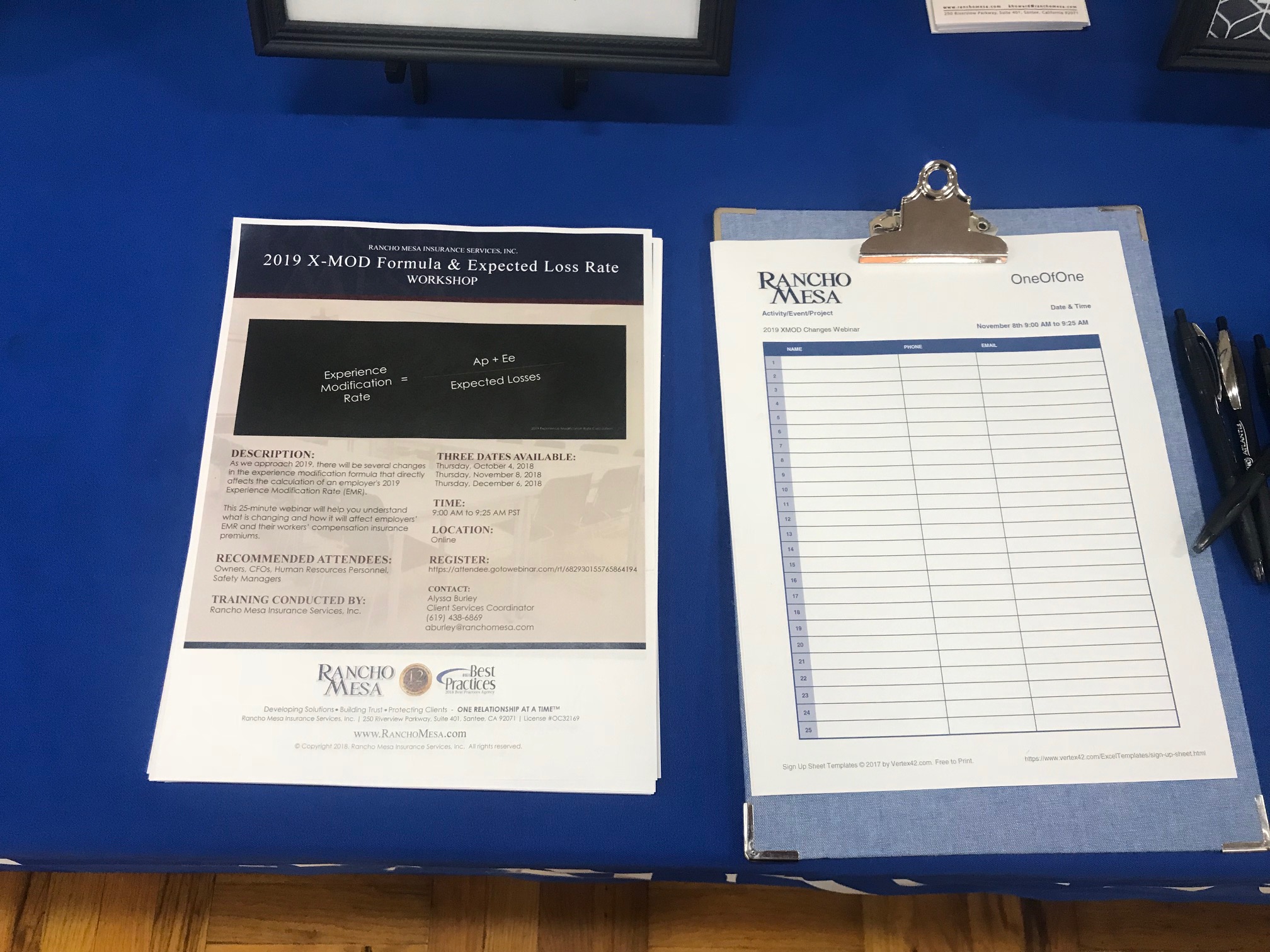 A flyer for the upcoming webinar and a clipboard with an empty sign in sheet laying on a table.