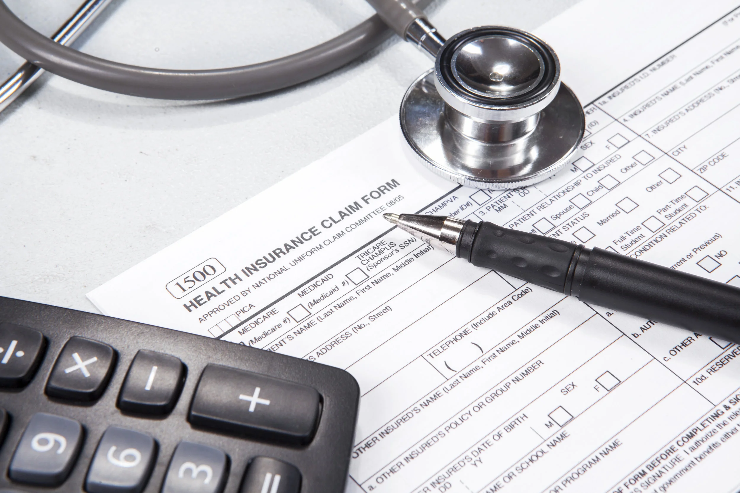 Health Insurance Claim Form, calculator, pen and stethoscope.