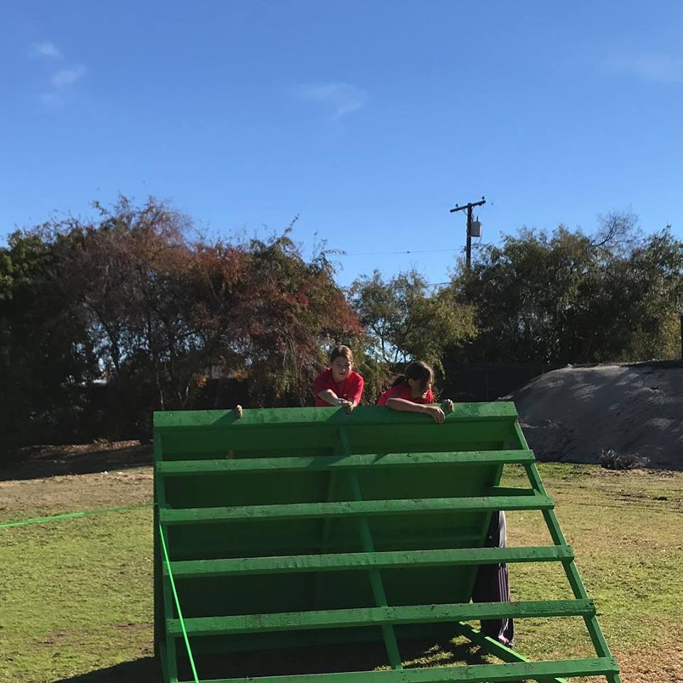 Trinity Restine and Kaia Hoolihan  climbing over a wall in the obstacle course. 