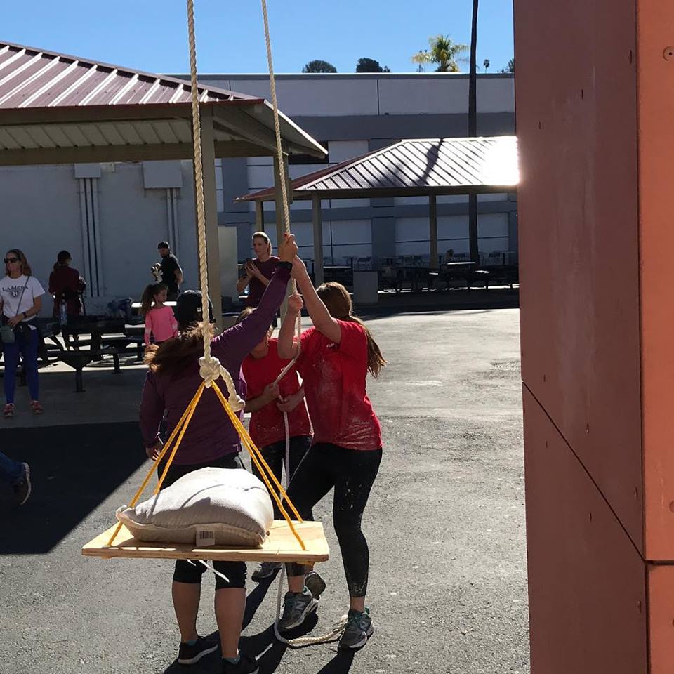 Trinity Restine and Kaia Hoolihan using a hoist (with a spotter) to lift a sandbag as a task in the obstacle course. 