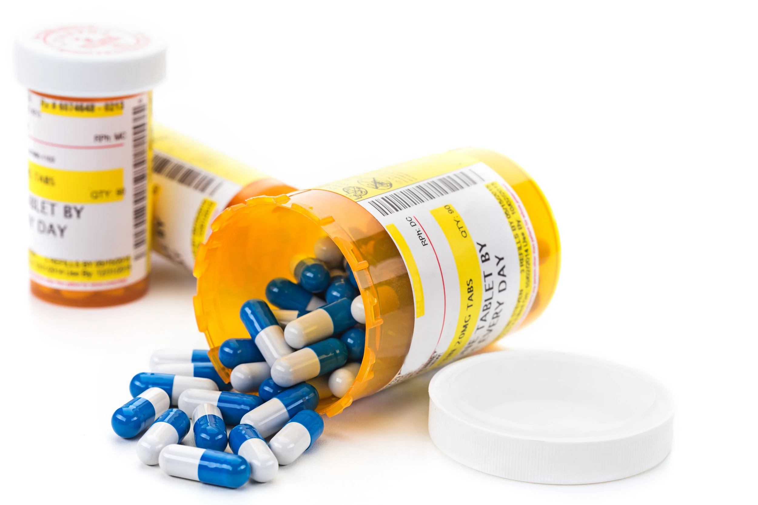 Three prescription pill bottles with one tipped over and the pills spilling out.