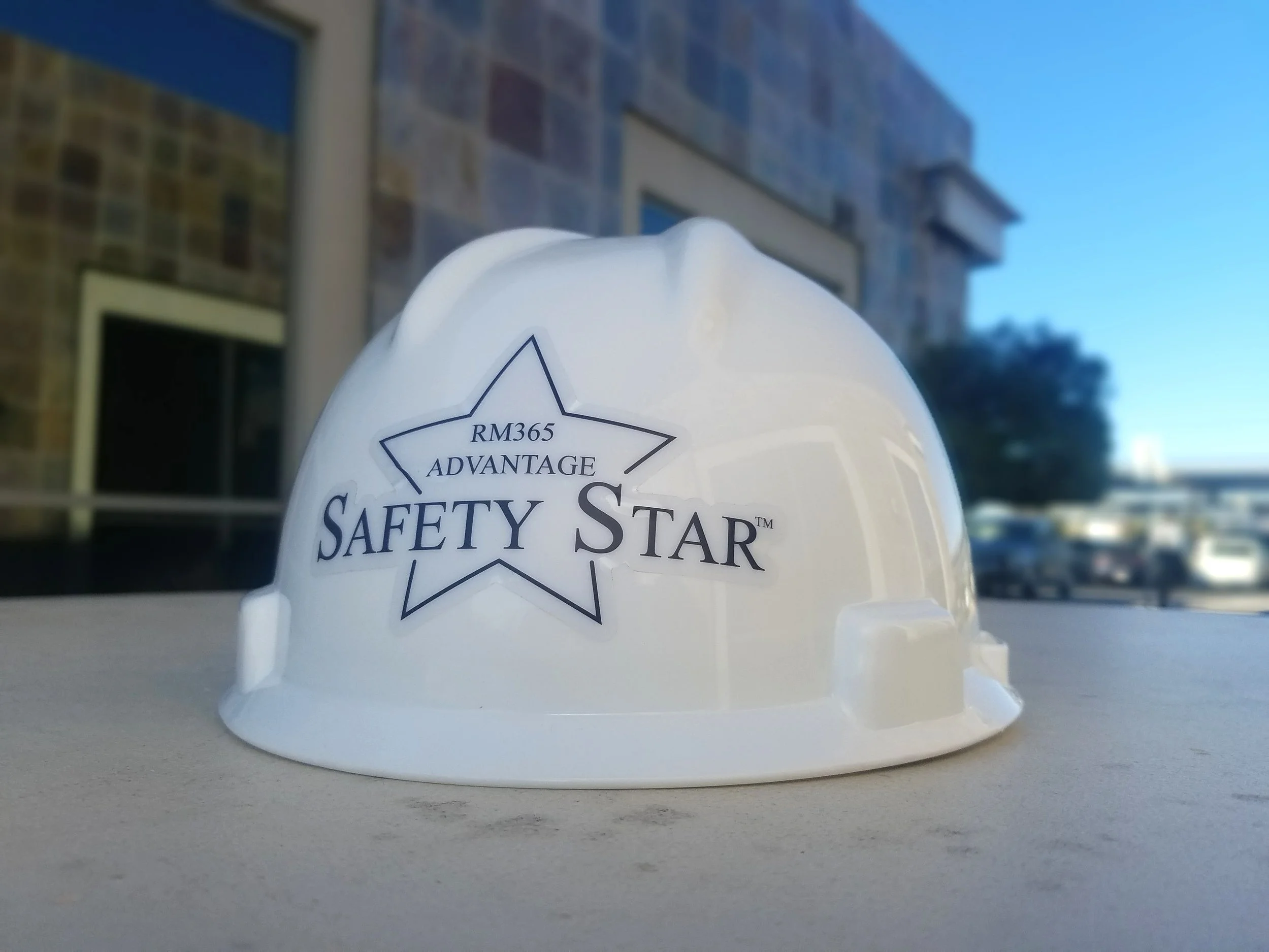 White hard hat sitting on an outdoor concrete table with a RM365 Advantage Safety Star sticker on the back.
